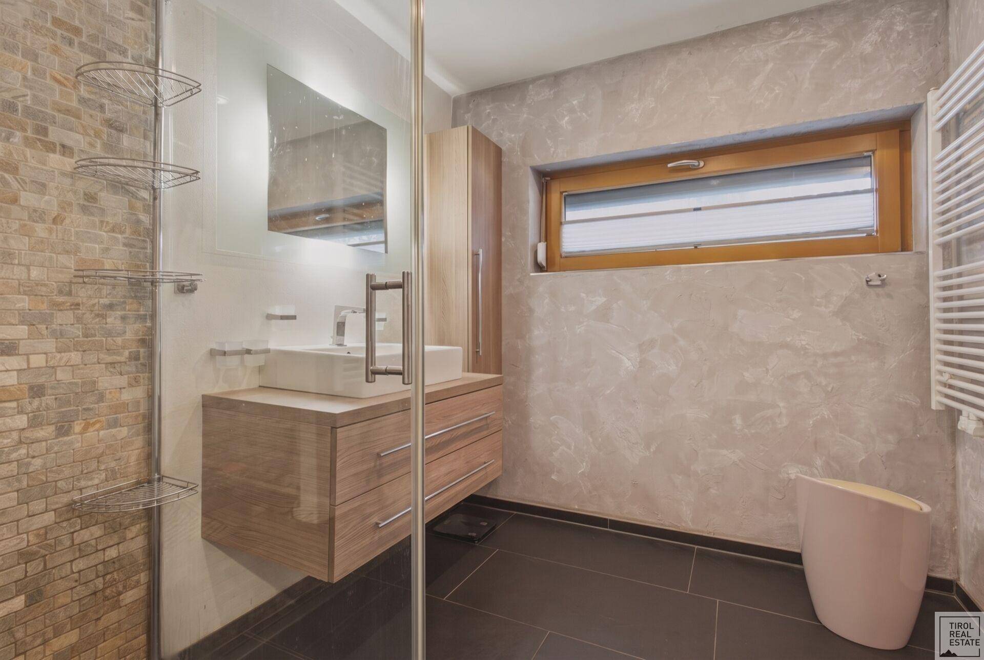 Badezimmer mit Dusche, Holzwaschtisch, beheiztem Handtuchhalter und Fenster.