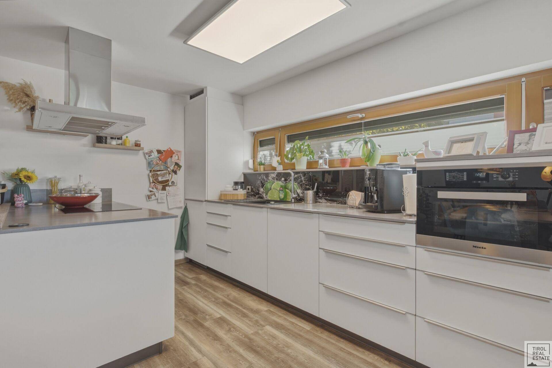 Moderne Einbauküche mit weißen Fronten, integrierten Geräten und großem Fenster.