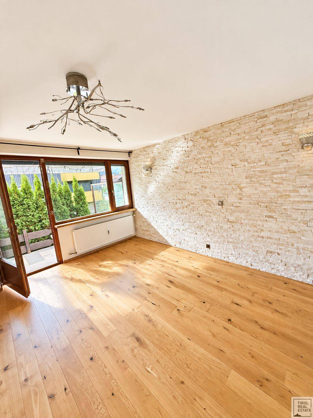 Heller Wohnraum mit Holzdielenboden, dekorativer Steinwand und direktem Zugang zum Außenbereich.