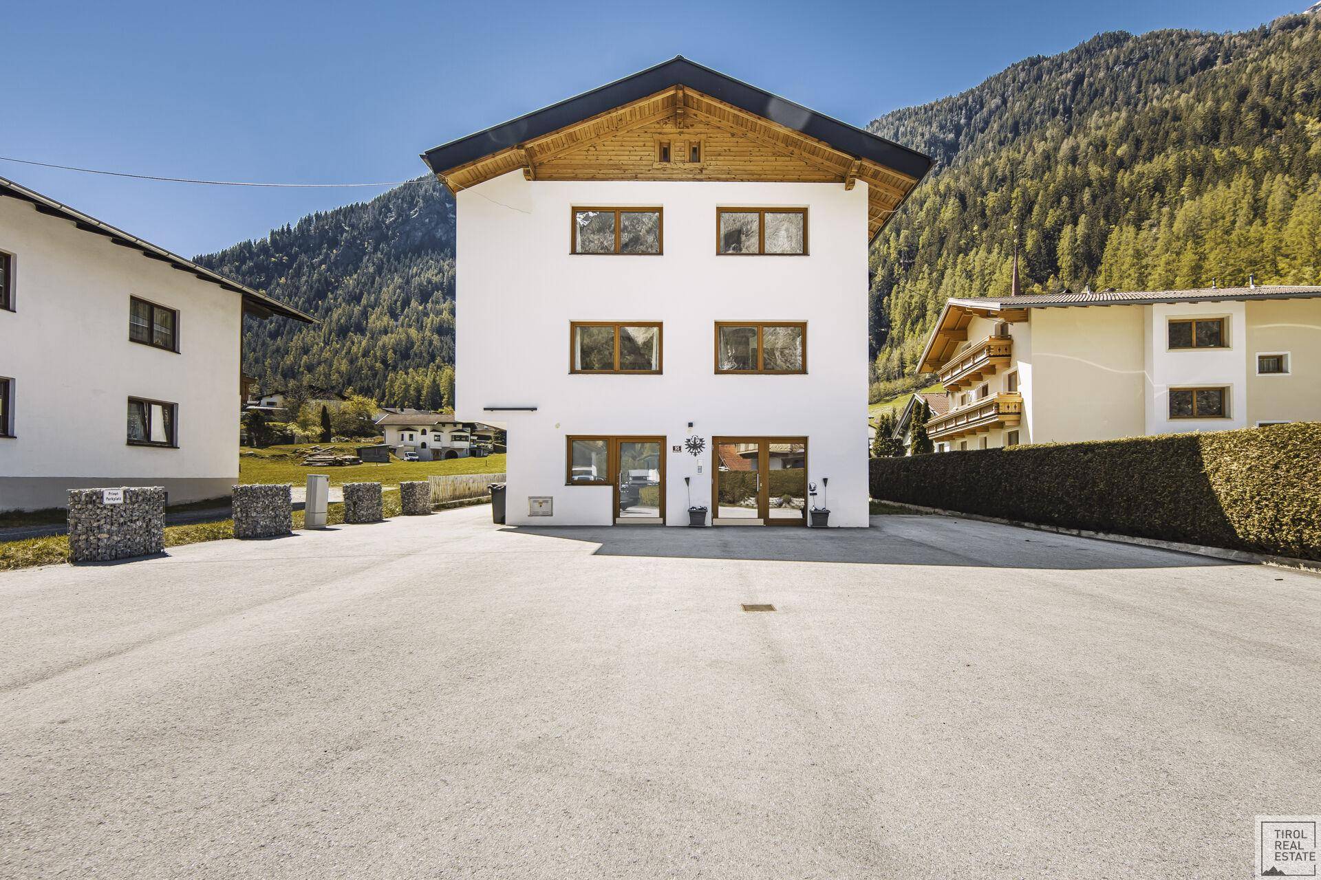 Vorderansicht des modernen Wohnhauses mit großem Parkplatz und traditionellem Holzdach.