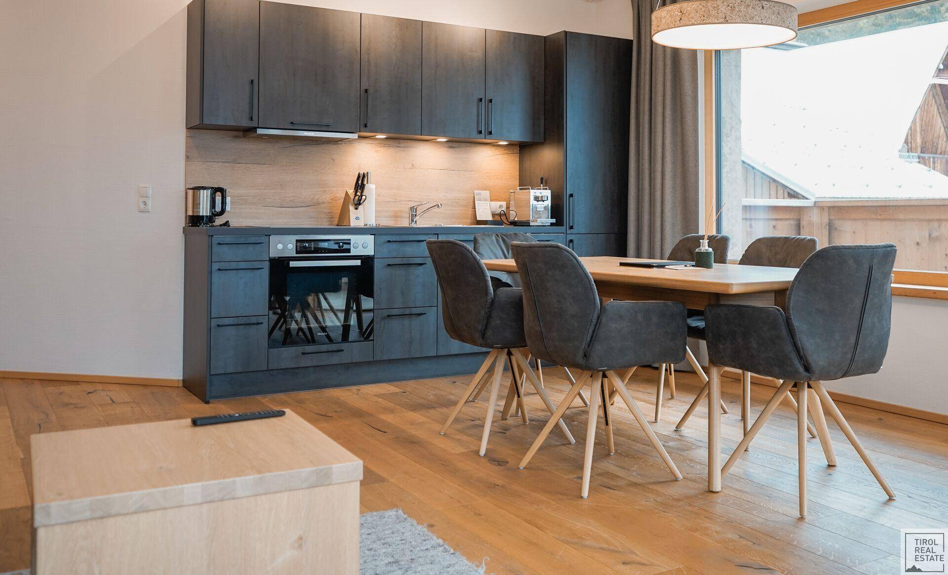 Heller Küchenbereich mit integriertem Essplatz, modernen grauen Fronten und Holzboden.