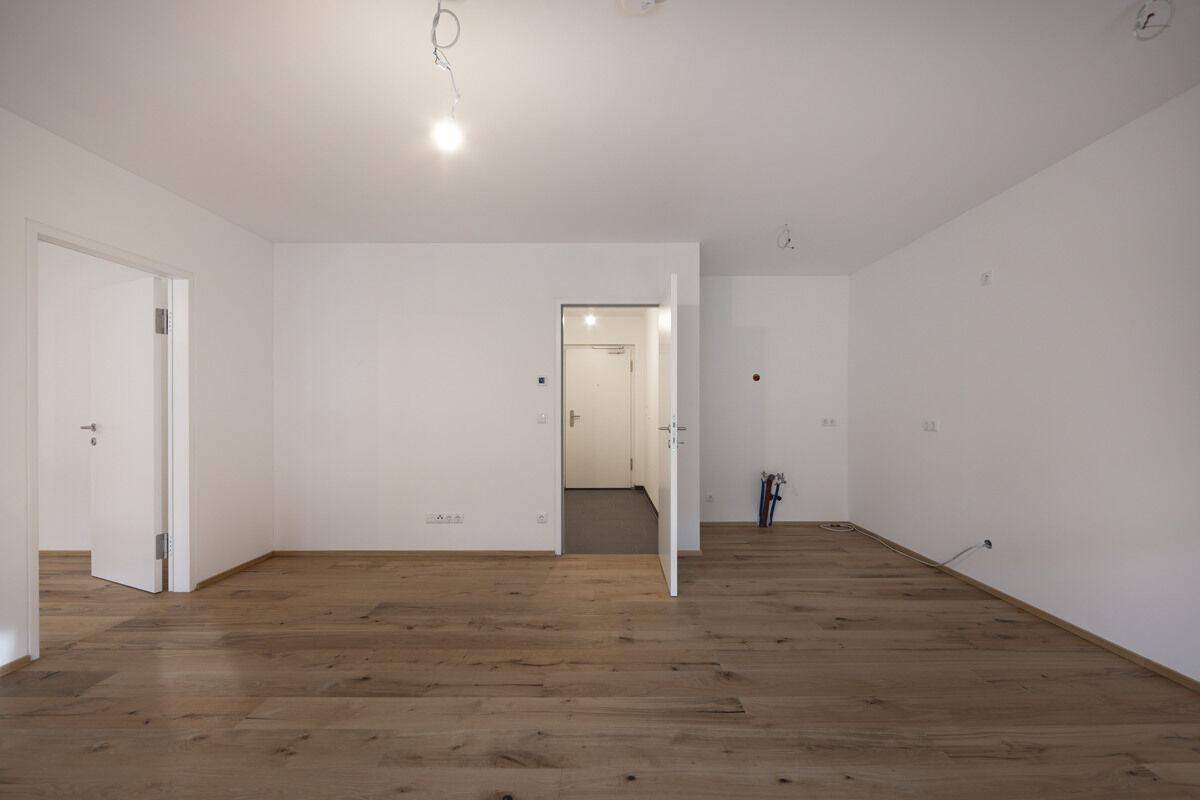 Helles, leeres Zimmer mit neuem Holzboden und weißen Wänden, bereit für die individuelle Gestaltung.