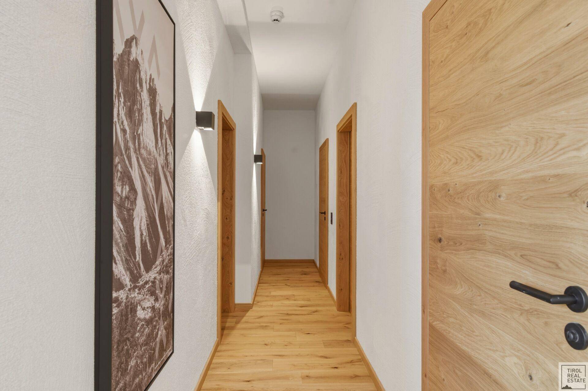 Heller Flur mit Holzboden und mehreren Türen, der zu den Zimmern führt.