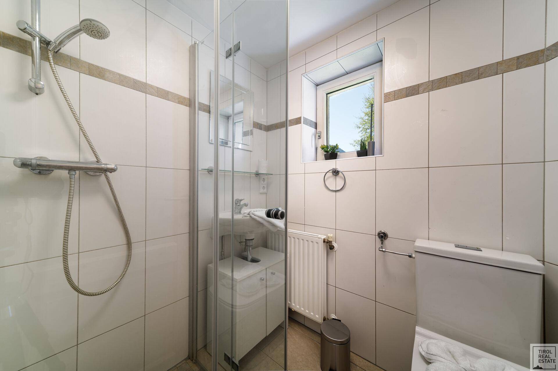Modernes Badezimmer mit Duschkabine, WC und Fenster für natürliche Belüftung.