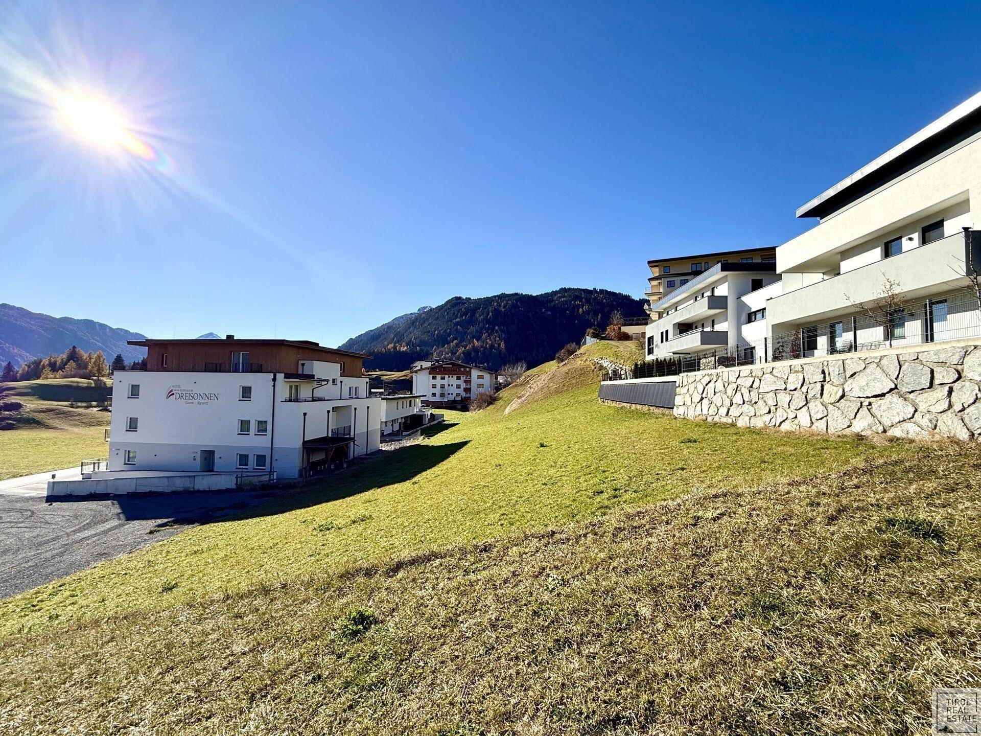 Panoramablick auf moderne Wohngebäude in einer sonnigen Hanglage mit weitreichender grüner Aussicht.