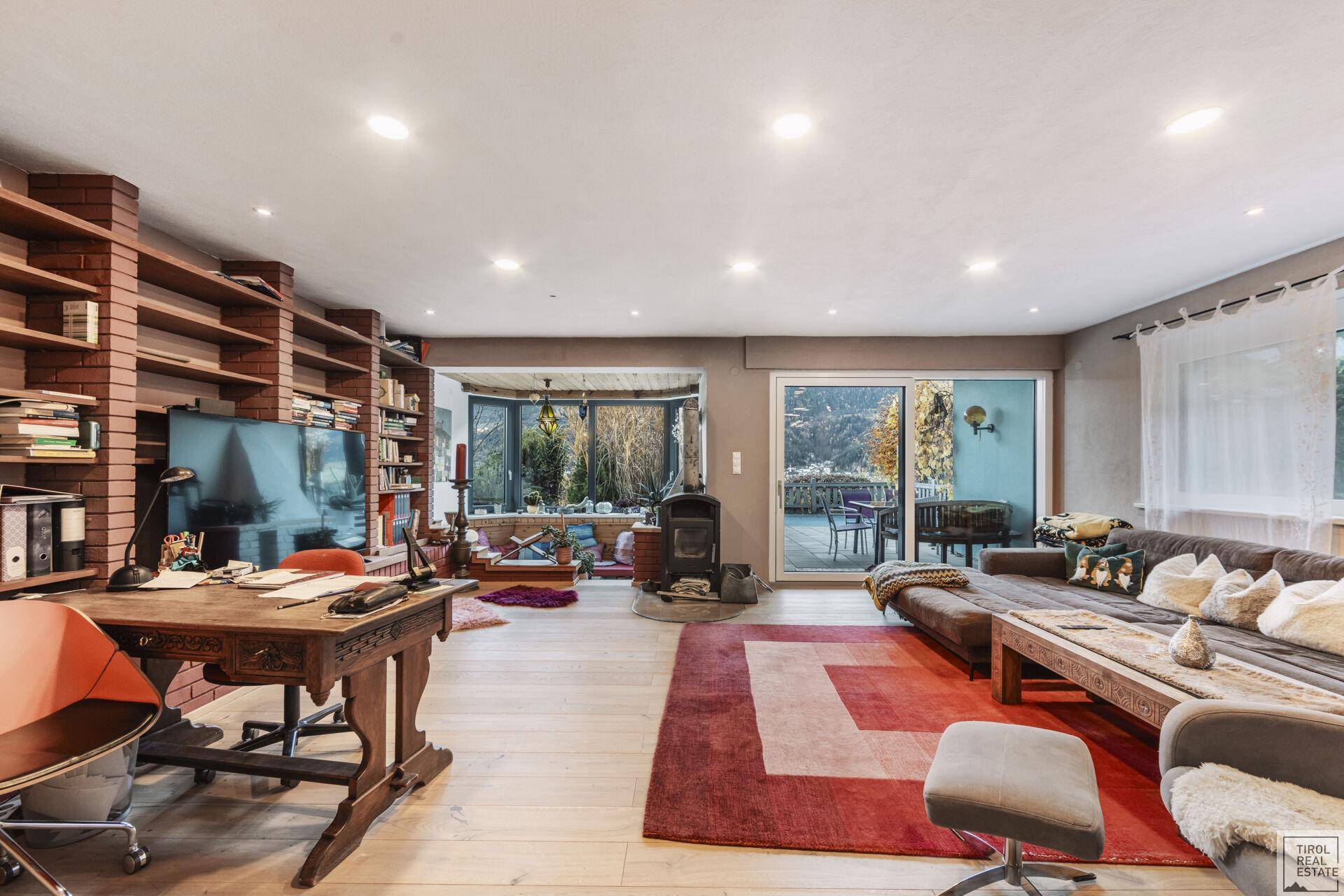 Geräumiges Wohnzimmer mit Holzboden, Bücherregalen und Blick ins Grüne.