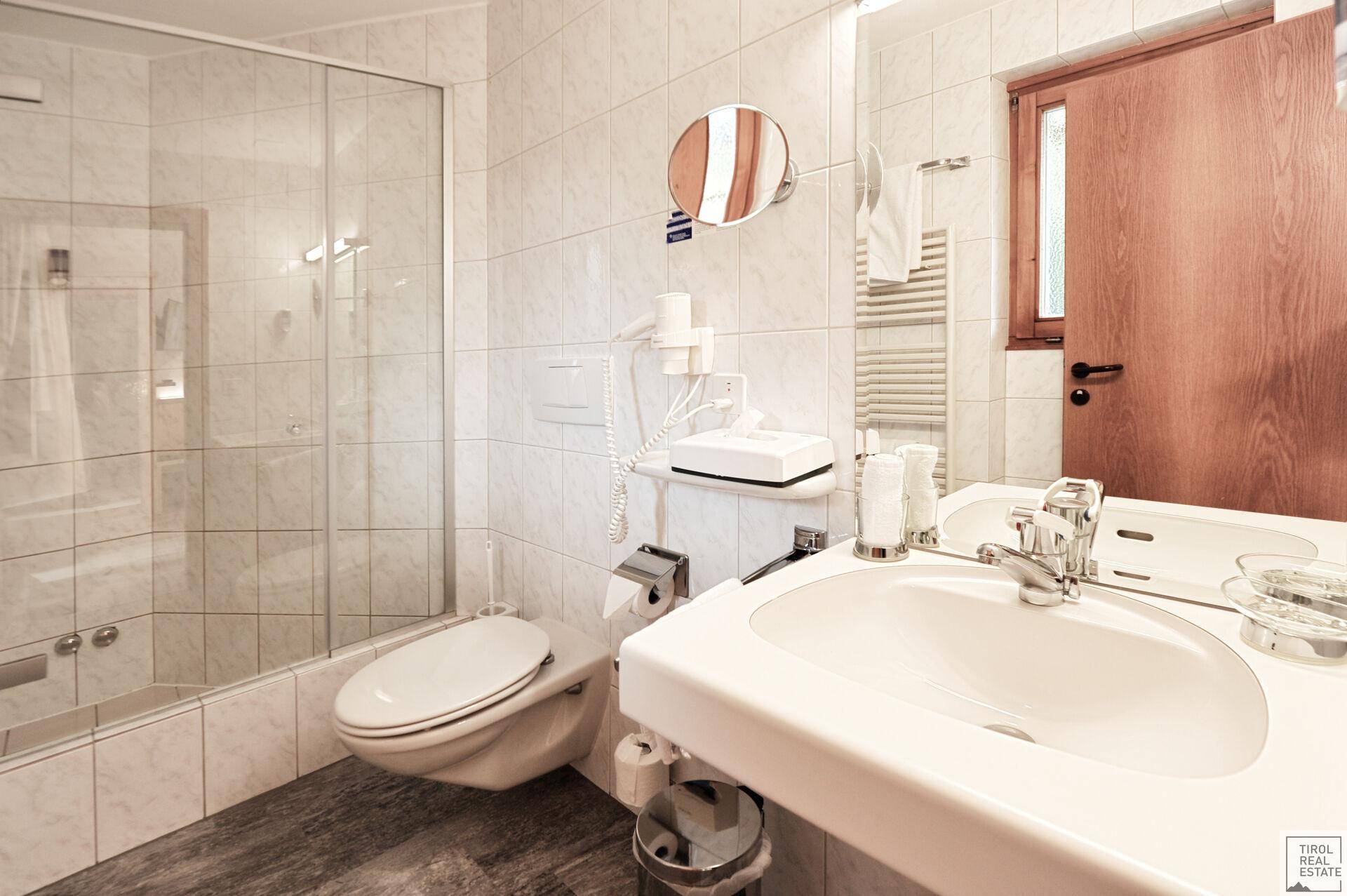 Badezimmer mit Badewanne, Duschabtrennung, WC und Waschbecken, alles in hellen Fliesen.