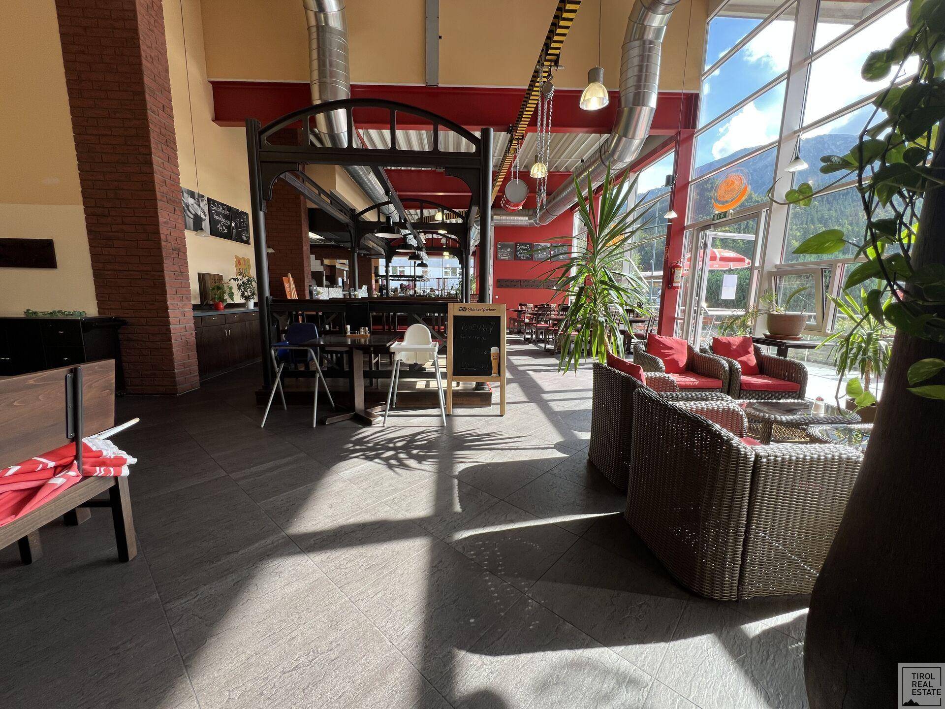 Gemütlicher Lounge-Bereich mit Korbmöbeln und großen Fenstern, die viel Tageslicht hereinlassen.