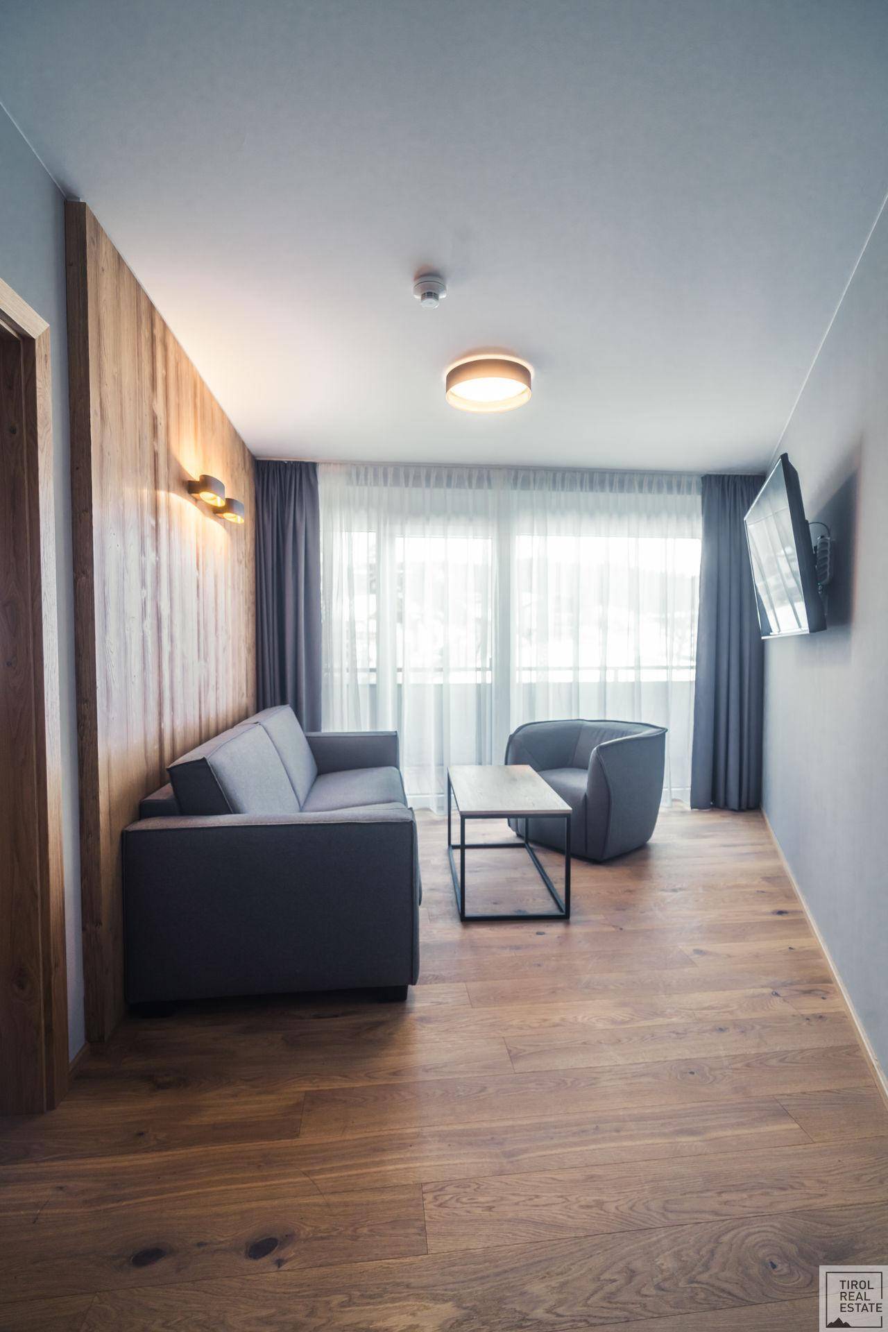 Helles Wohnzimmer mit Holzboden, bequemen Sitzmöbeln und großen Fenstern.