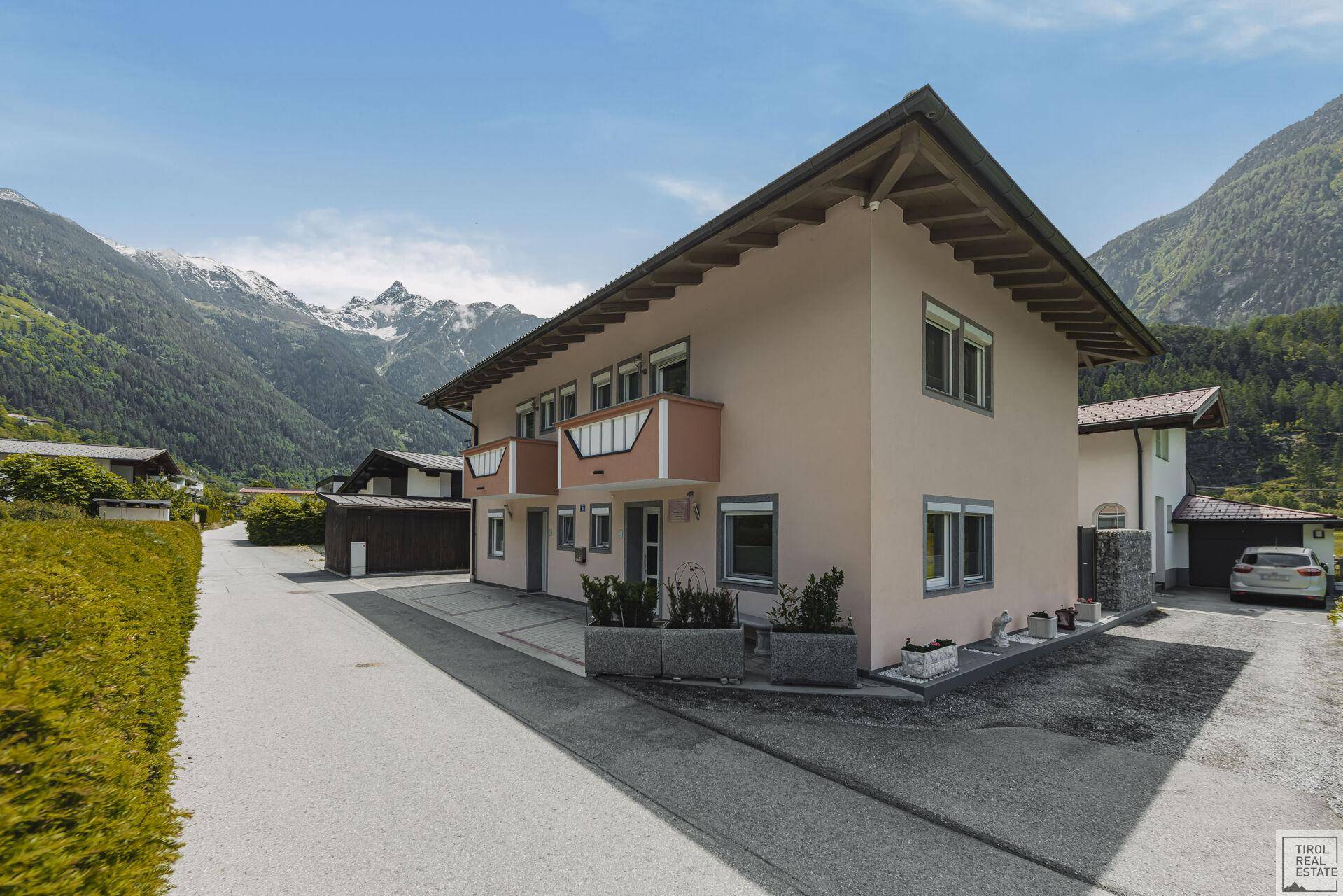 Seitenansicht des Wohnhauses mit Balkonen und Blick auf die umliegende Berglandschaft.