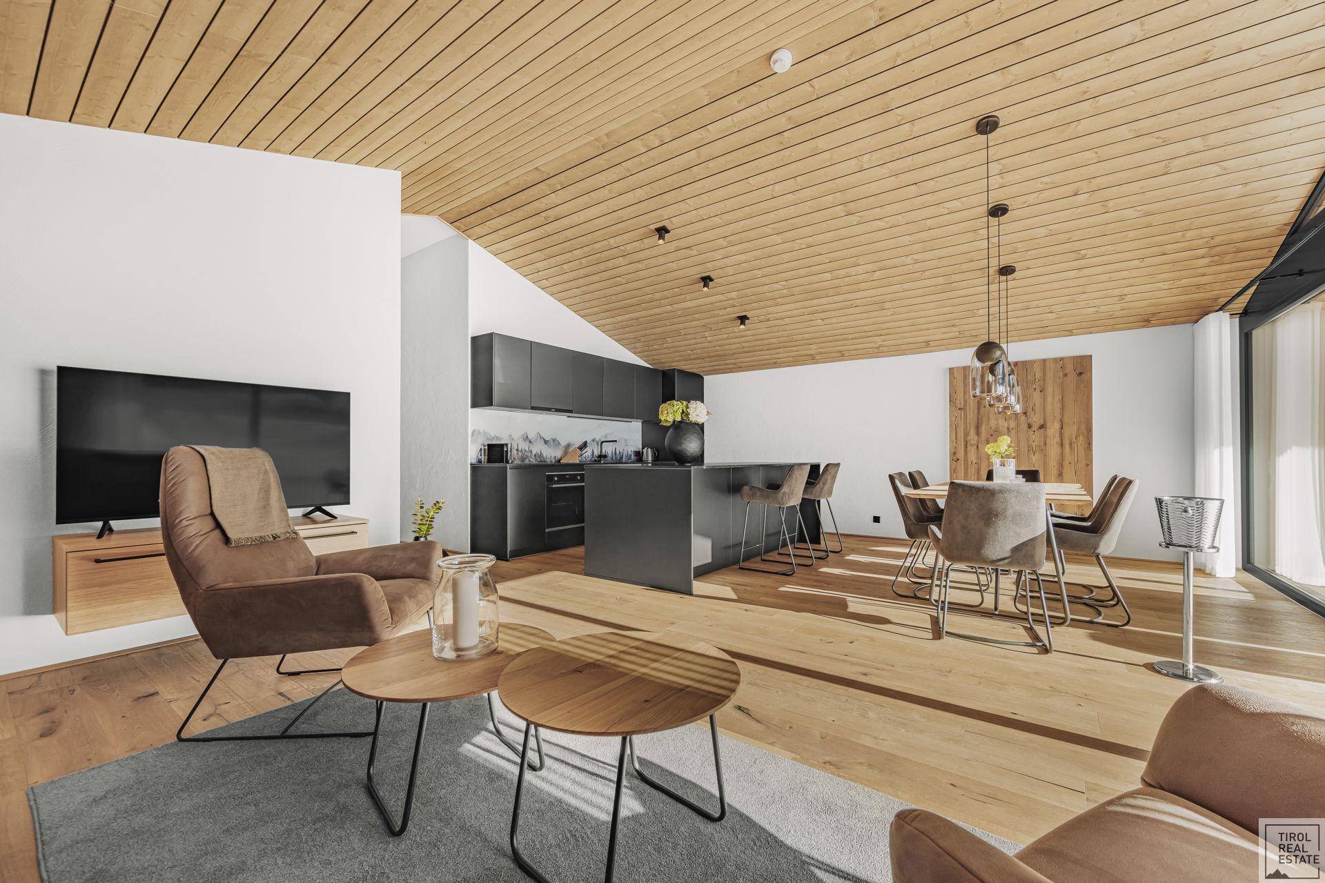Geräumiger offener Wohn-Essbereich mit Holzboden, moderner Küche und gemütlicher Sitzecke unter einer Holzdecke.