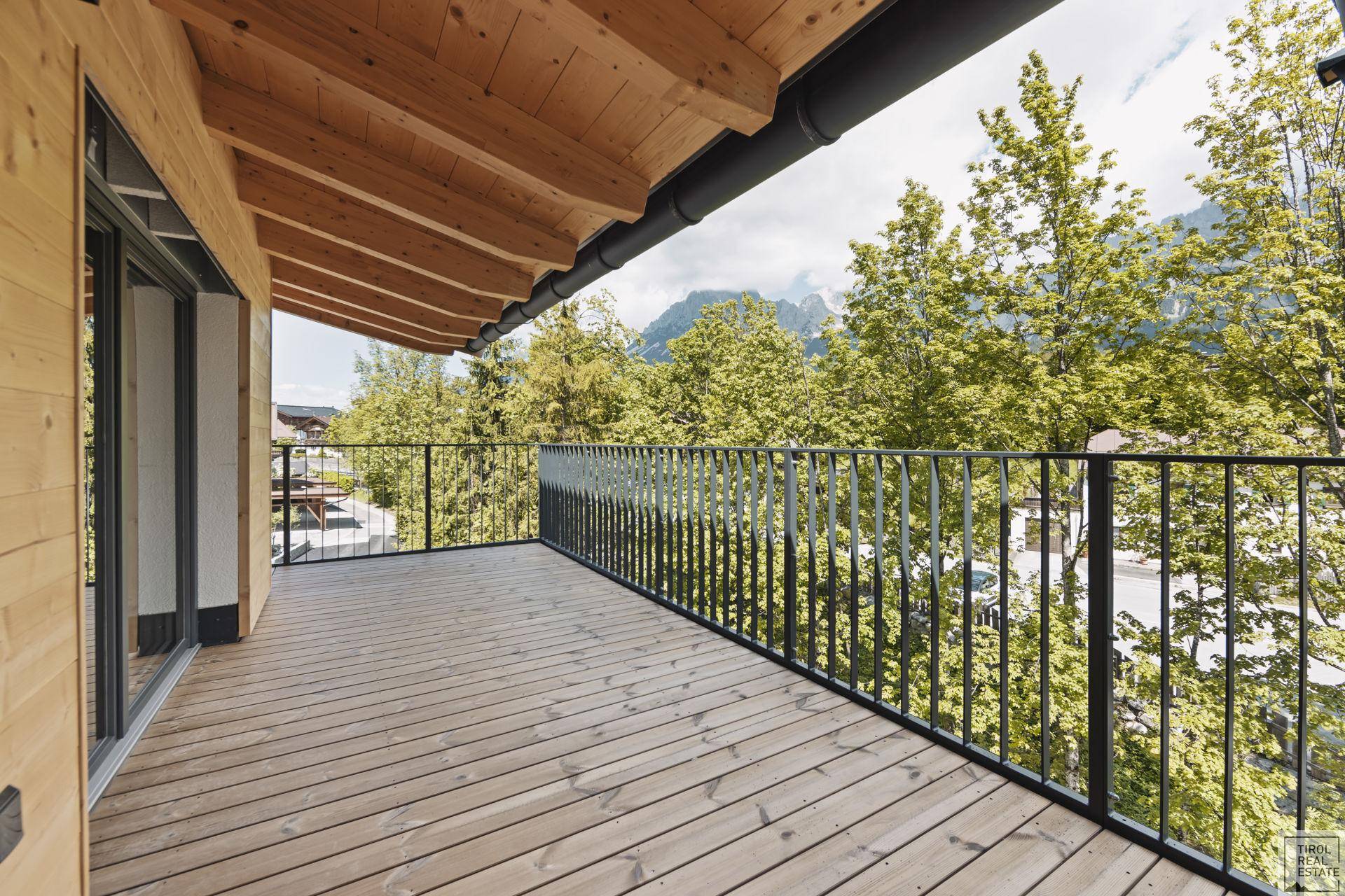 Langer Holzbalkon mit schwarzem Geländer und weitem Blick auf die umliegenden Berge.