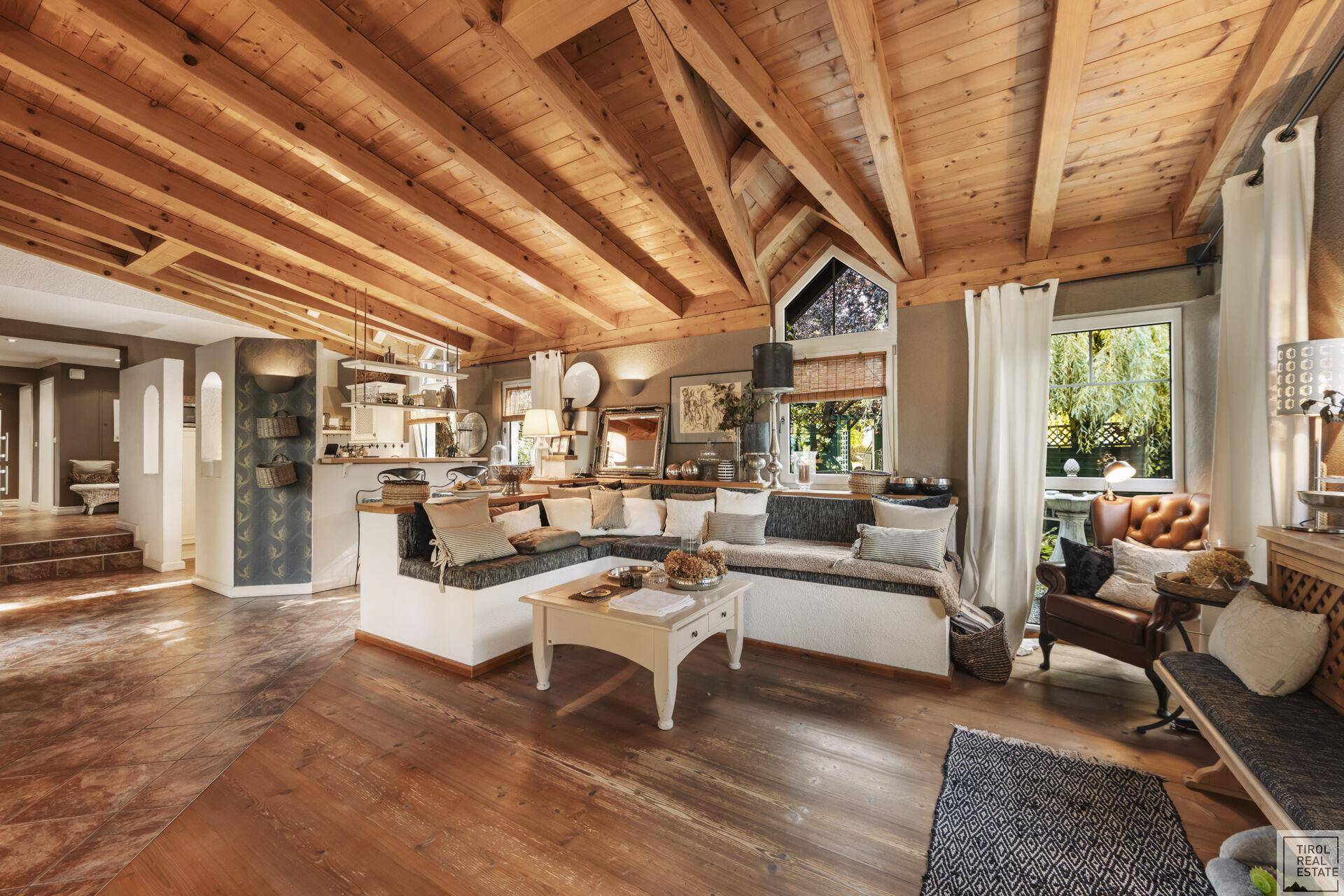Geräumiges Wohnzimmer mit beeindruckender Holzbalkendecke, gemütlicher Sitzecke und Holzboden.