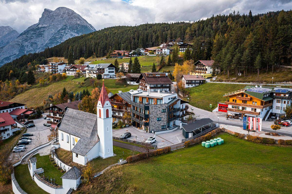 Luftaufnahme eines charmanten Bergdorfes mit traditionellen und modernen Gebäuden in alpiner Landschaft.