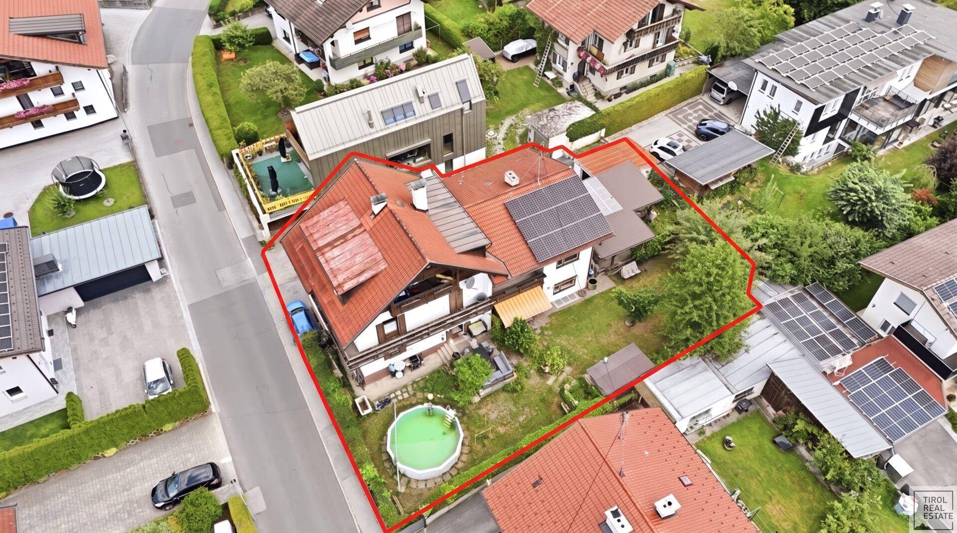 Luftaufnahme eines gepflegten Hauses im Chalet-Stil mit Garten, Pool und Photovoltaikanlage auf dem Dach.