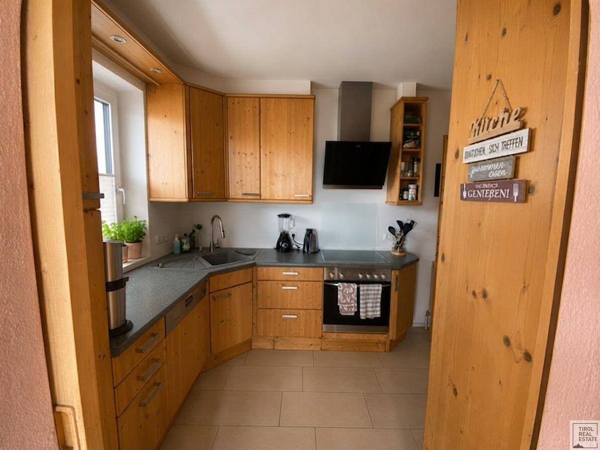Funktionale Küche mit hellen Holzschränken, dunklen Arbeitsplatten und einem Fenster, das Tageslicht hereinlässt.