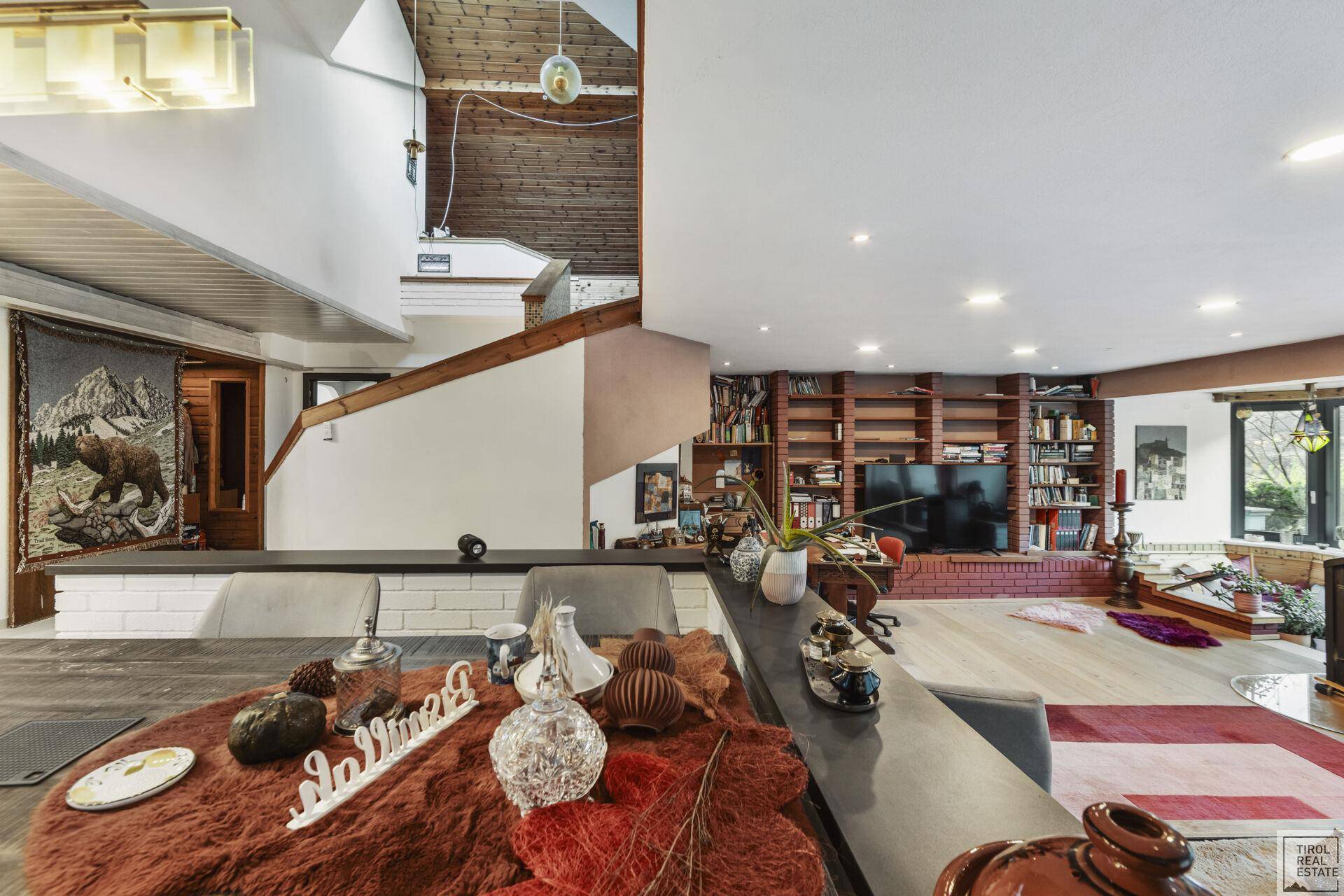 Offener Wohnbereich mit Holzbalkendecke, Treppe und integrierten Bücherregalen.