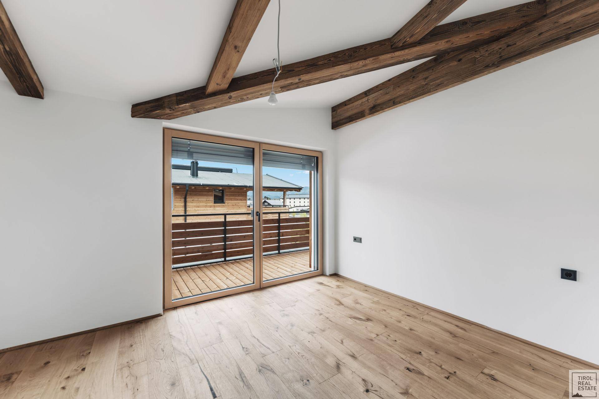 Helles Zimmer mit Holzbalken, Parkettboden und Zugang zu einem Balkon oder einer Terrasse.