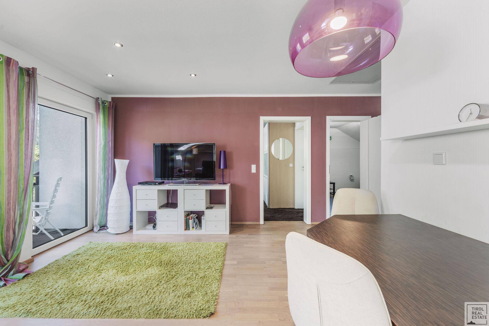 Wohnbereich mit Fernseher, farbenfroher Dekoration und Zugang zu einem Balkon.