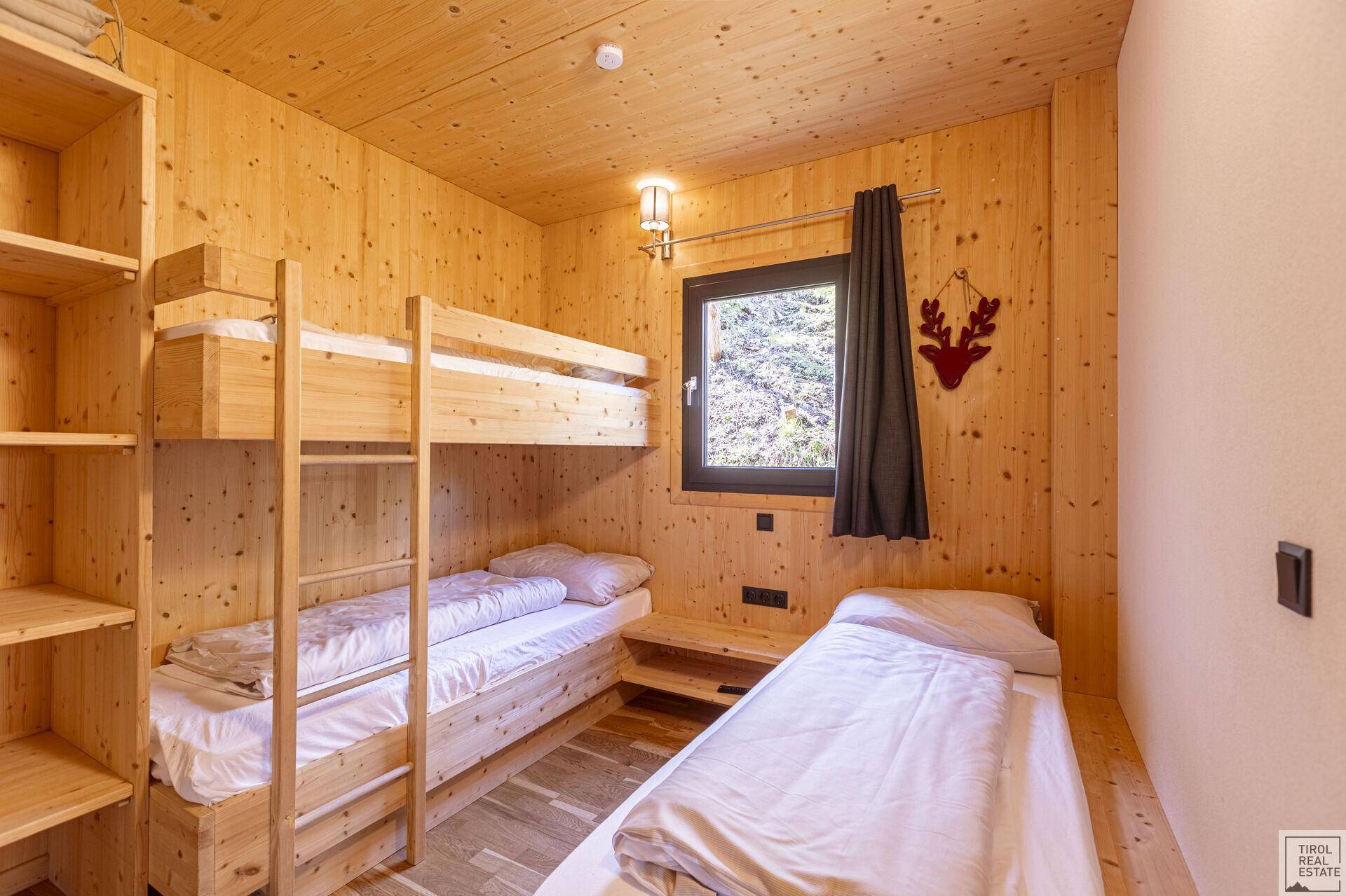 Kinderzimmer mit Etagenbett, Einzelbett und Holzwänden im alpinen Stil.