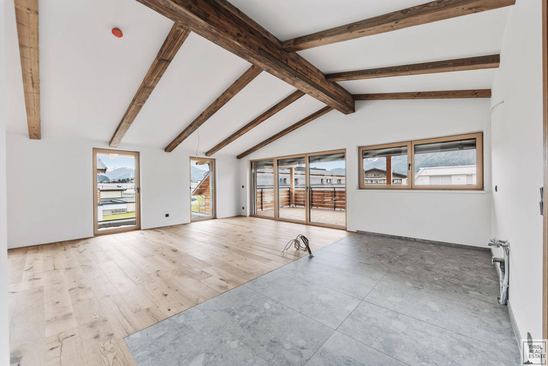 Heller, unmöblierter Raum mit Holzbalken, Parkettboden und Zugang zu einer Terrasse.