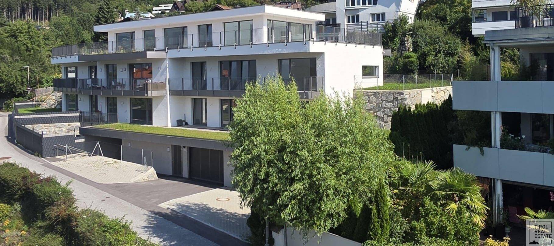 Moderne Wohnanlage mit weißer Fassade, Balkonen und begrüntem Dach in grüner Umgebung.