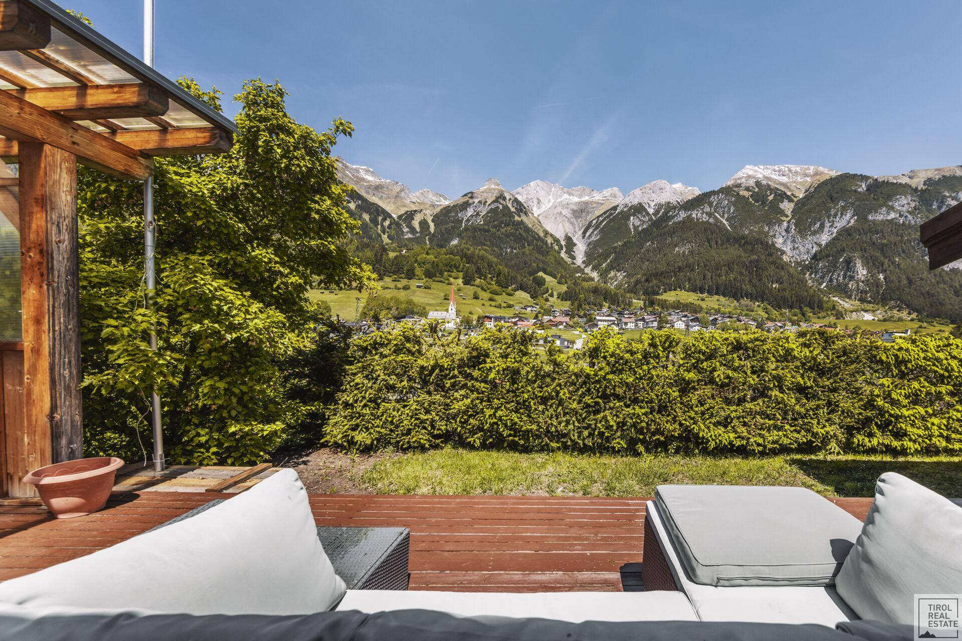 Entspannungsbereich auf der Holzterrasse mit Lounge-Möbeln und Panoramablick auf die Berge.