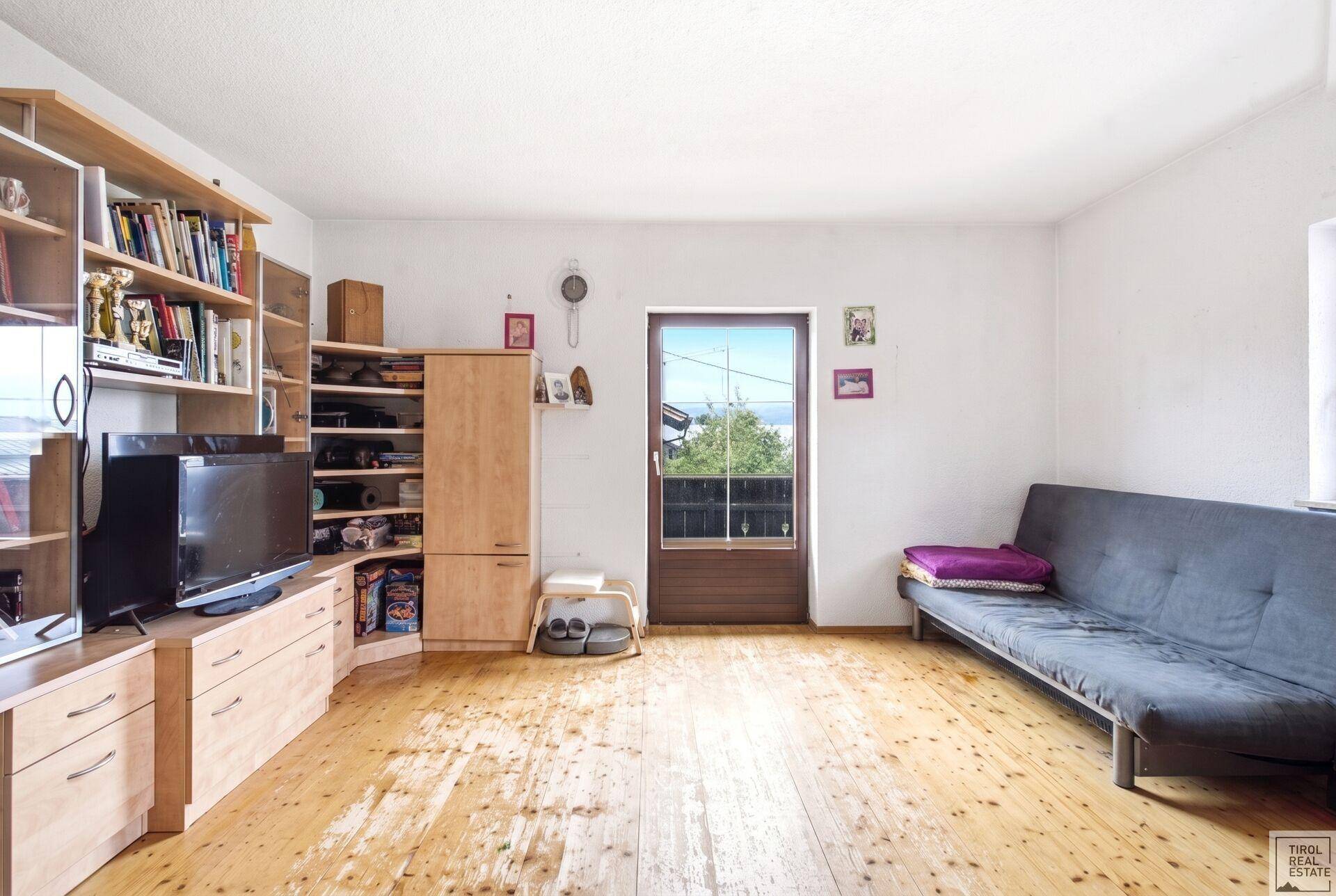 Helles Zimmer mit Holzplankenboden, Regalen und Zugang zu einem Balkon.