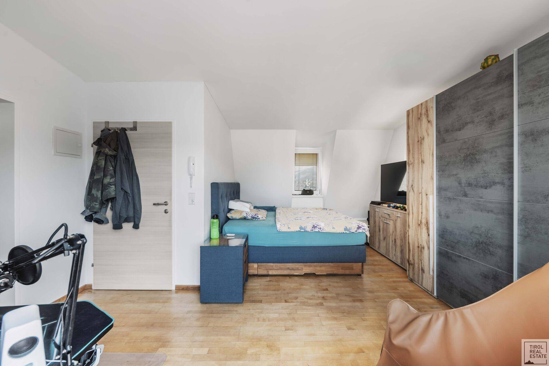Helles Dachgeschoss-Schlafzimmer mit Holzboden, Schrank und gemütlicher Atmosphäre.