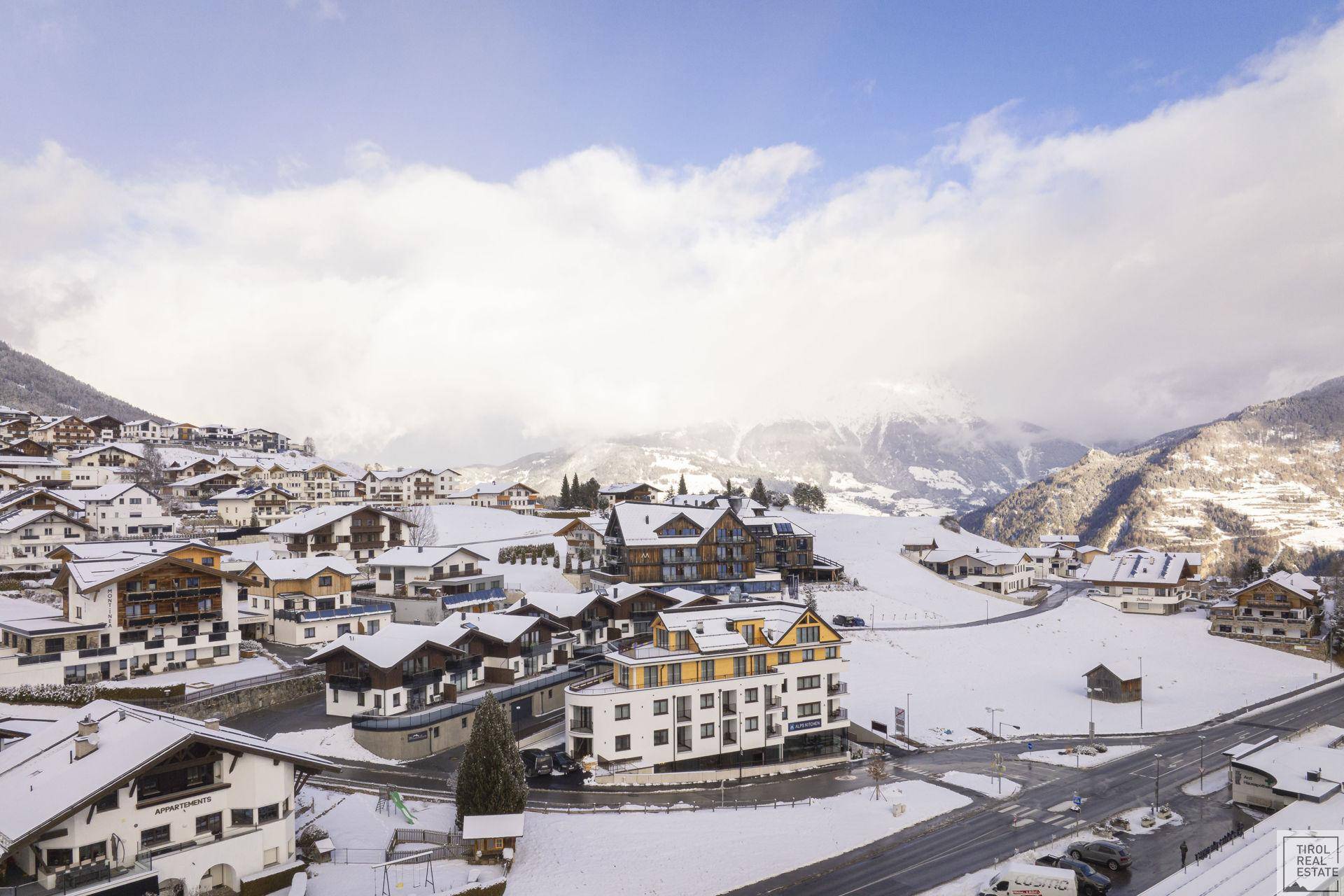 Panoramablick auf ein verschneites Bergdorf mit modernen Gebäuden und traditionellen Häusern.