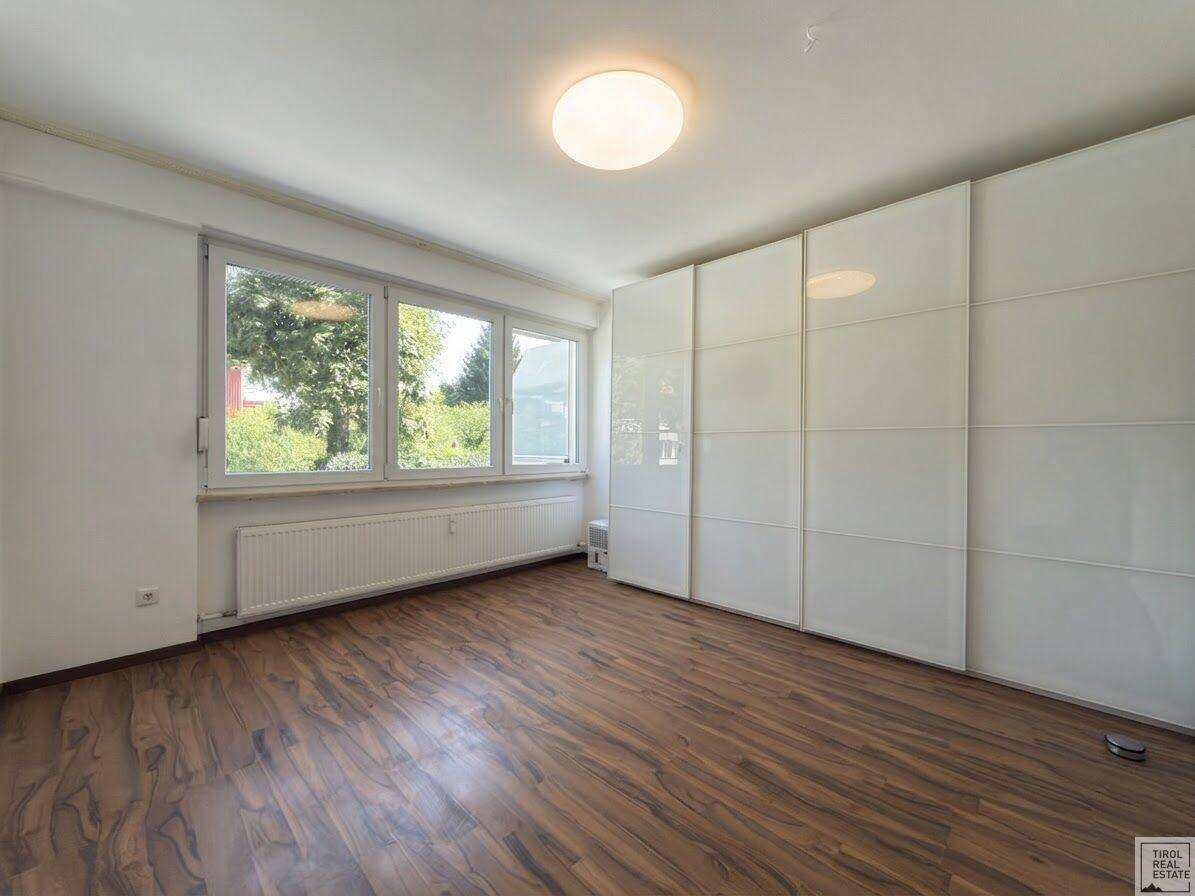 Schlafzimmer mit großem Einbauschrank, Holzboden und Fenstern mit Blick ins Grüne.