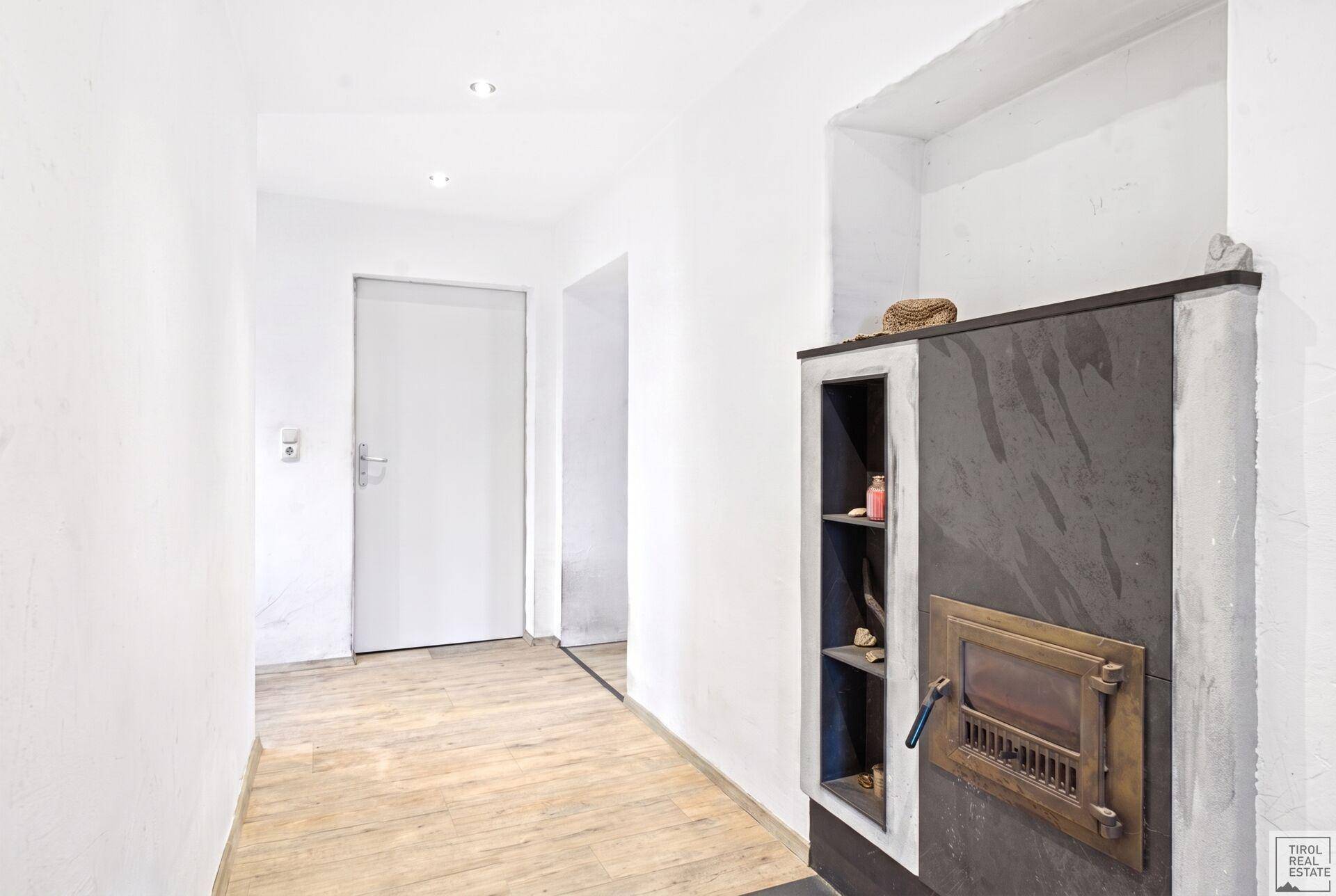 Heller Flur mit traditionellem Kachelofen und modernem Holz-Look-Boden.