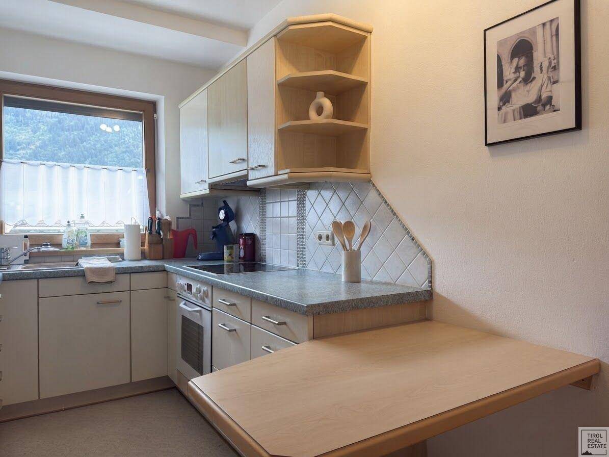 Detailansicht der Küche mit Spüle, Herd, gefliestem Spritzschutz und praktischem Klapptisch.
