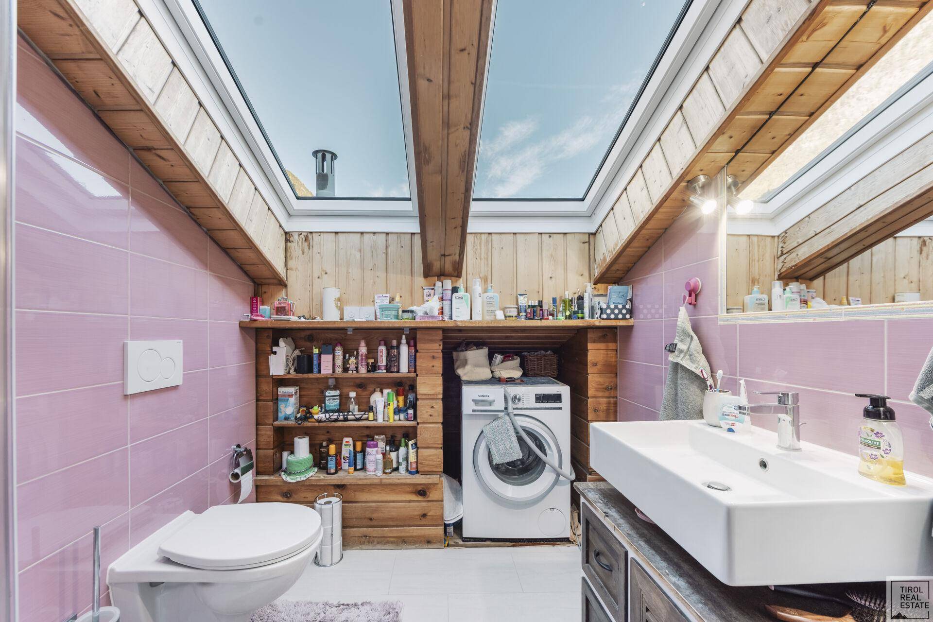 Modernes Badezimmer mit rosa Fliesen, Waschmaschine und Dachfenstern für viel Licht.