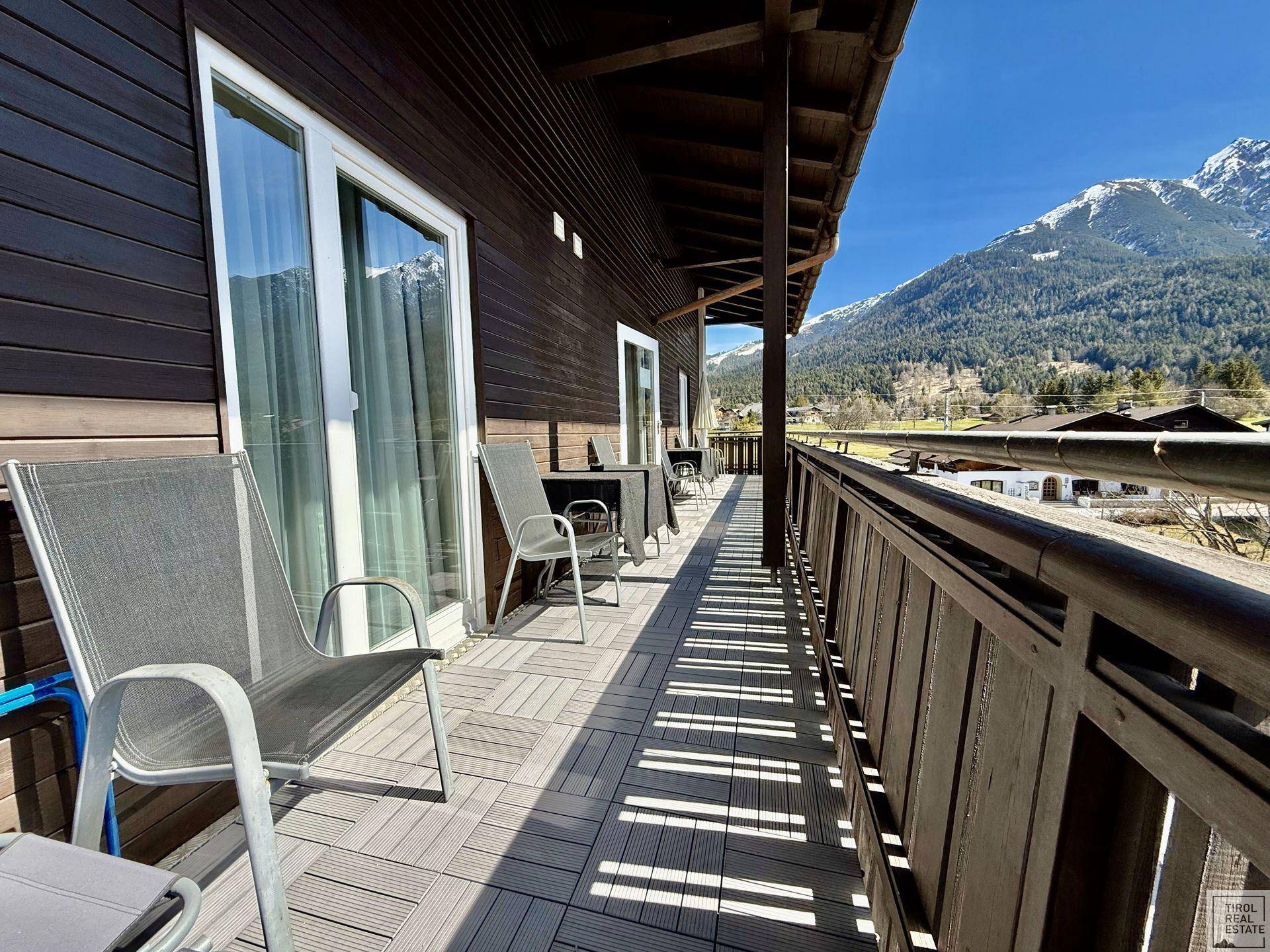 Langer Holzbalkon mit Sitzgelegenheiten und weitem Blick auf die Berge.