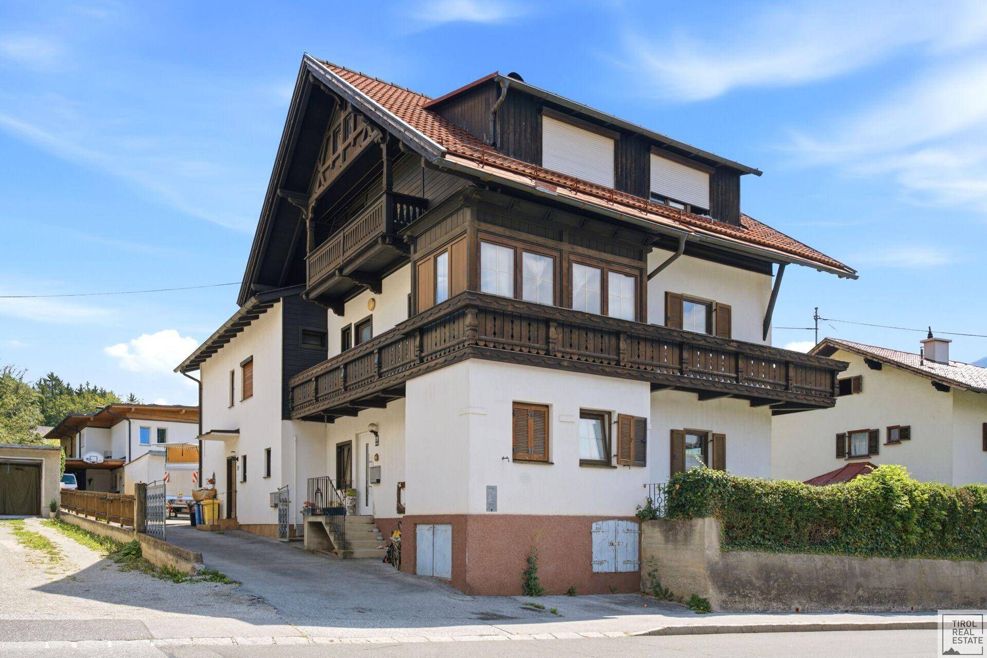 Traditionelles Haus im alpinen Stil mit Holzbalkonen und weißer Fassade unter blauem Himmel.