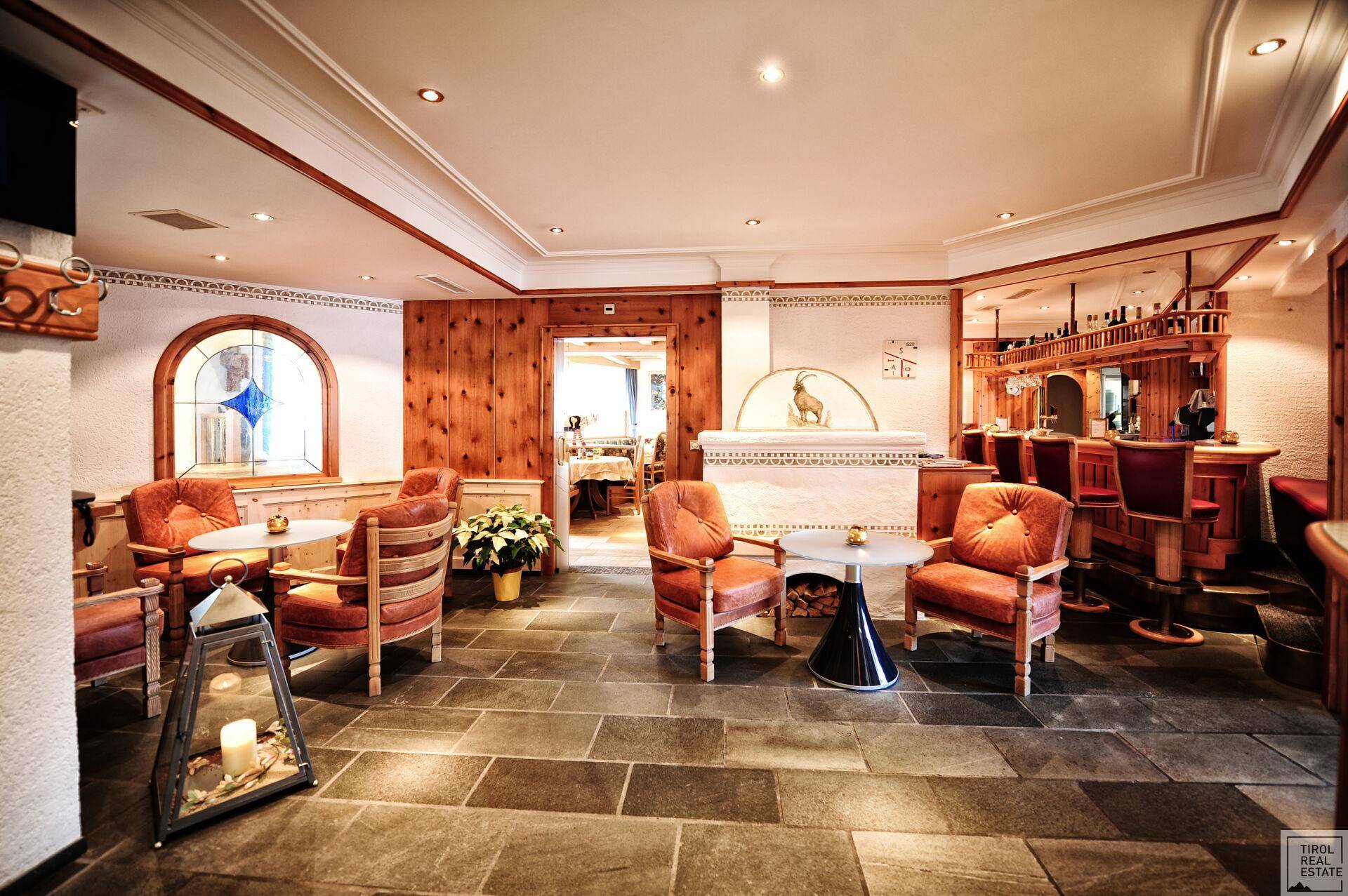 Geräumiger Loungebereich mit Steinfliesenboden, Holzvertäfelung und einer gut ausgestatteten Bar im Hintergrund.