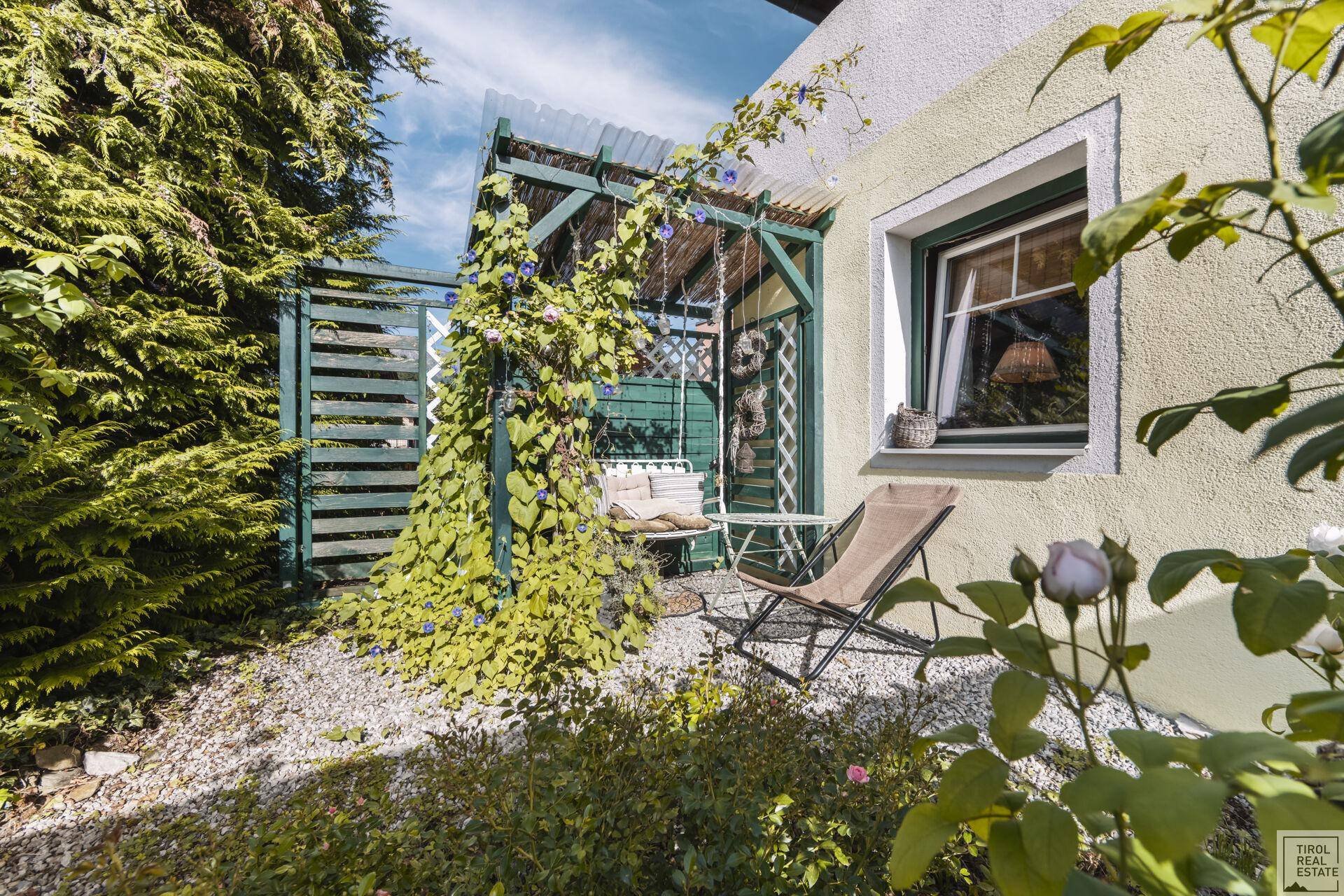 Kleiner, lauschiger Gartenbereich mit Schaukelbank unter einer Pergola und Liegestuhl.