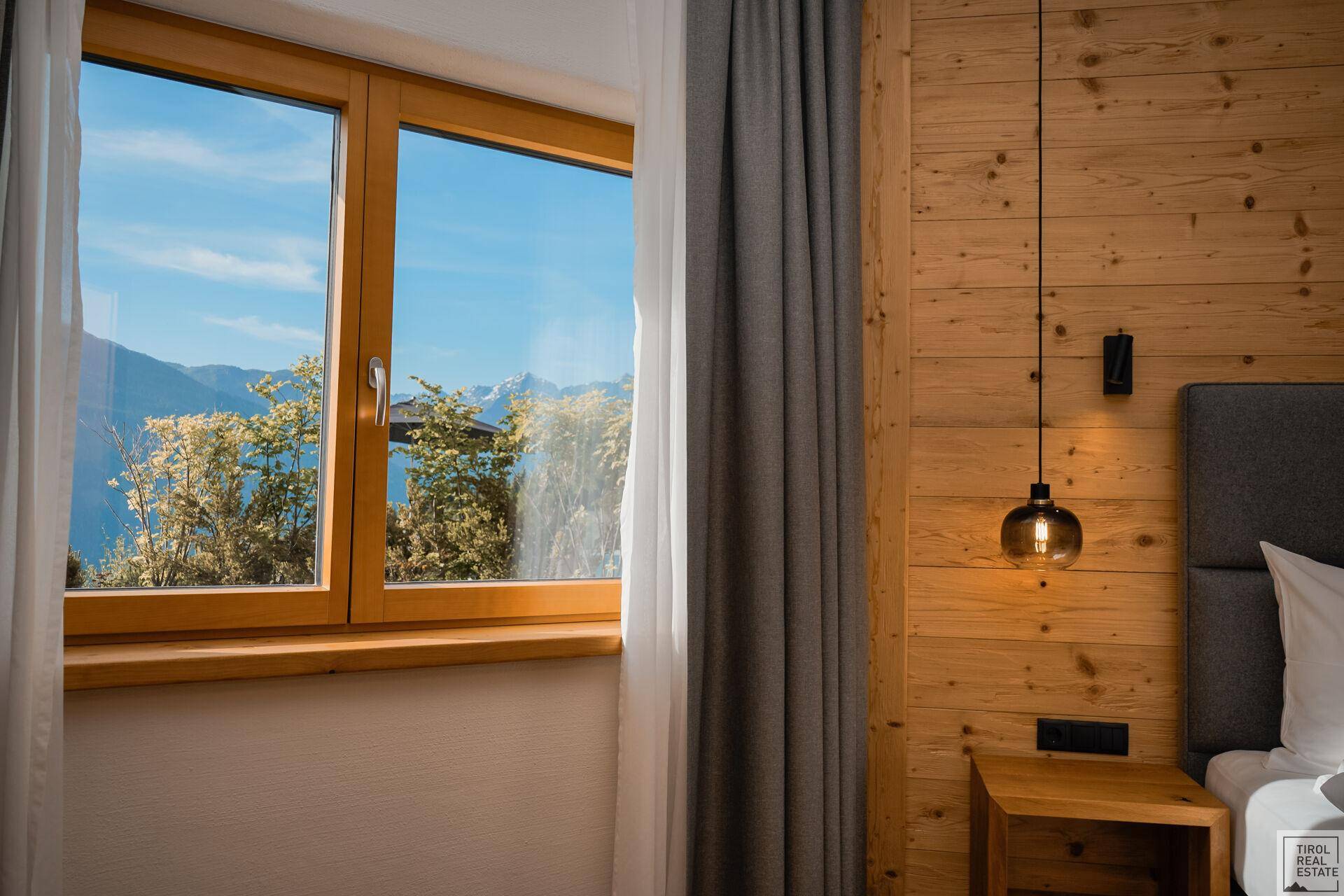 Schlafzimmerfenster mit herrlichem Blick auf die sonnige Berglandschaft und blauen Himmel.