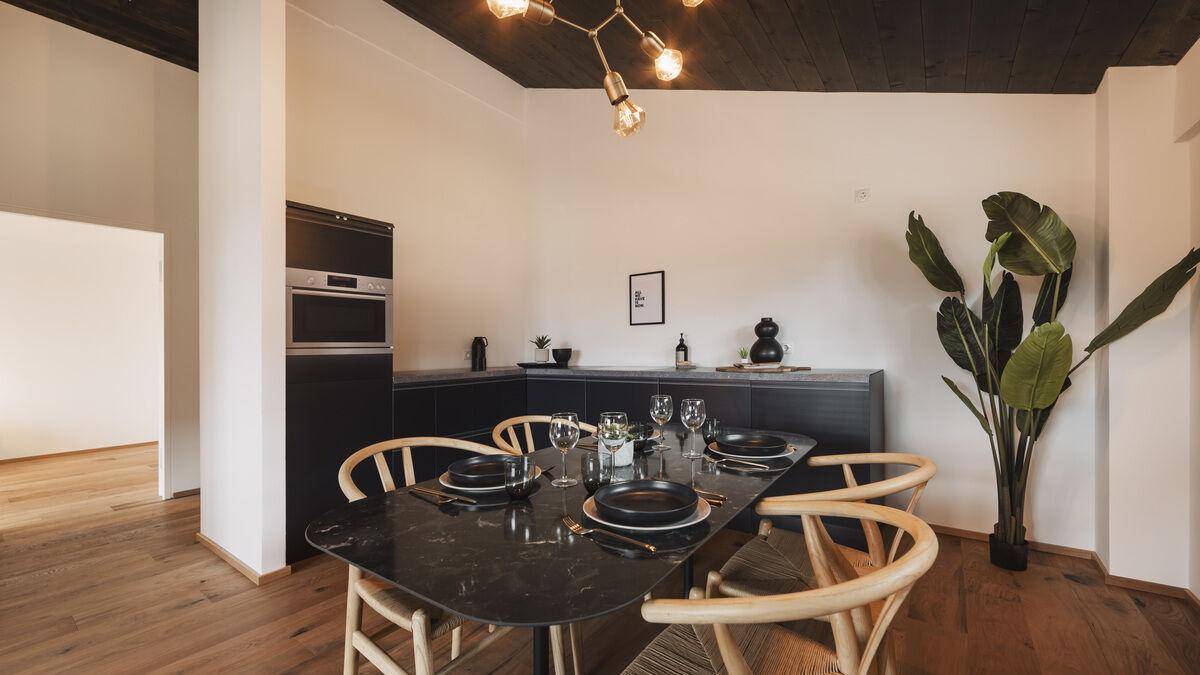 Eleganter Essbereich mit dunklem Tisch, Holzboden und integrierter Küchenzeile.