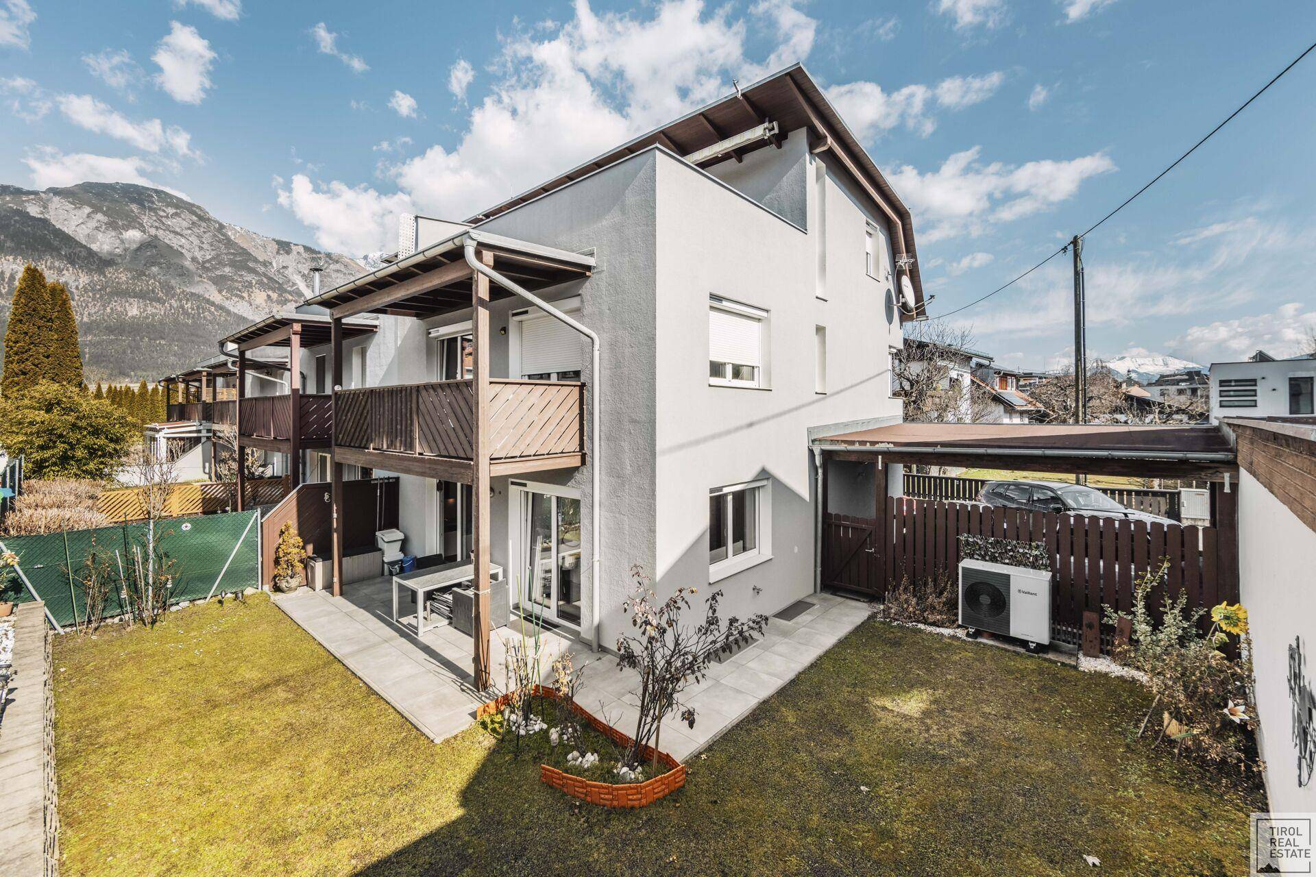 Außenansicht des Hauses mit gepflegtem Garten, Terrasse und Bergblick unter blauem Himmel.