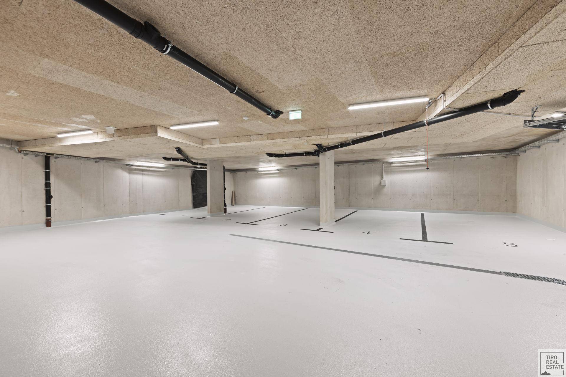 Moderne Tiefgarage mit Betonwänden, sichtbaren Leitungen und markierten Stellplätzen für Fahrzeuge.