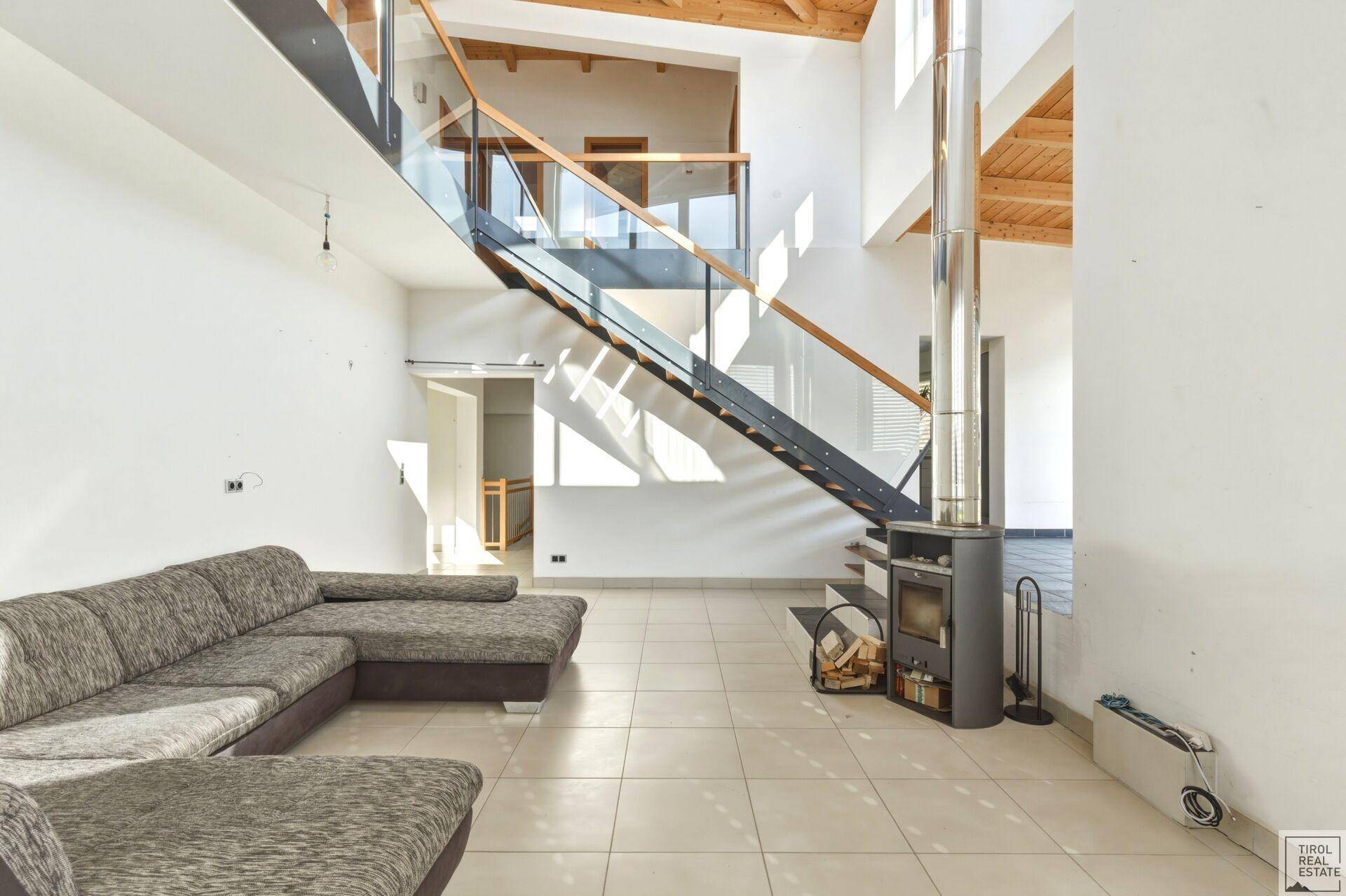 Geräumiger Wohnbereich mit Kaminofen, moderner Treppe und hohen Decken, ideal für Entspannung.