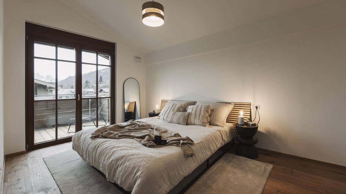 Helles Schlafzimmer mit Doppelbett, Holzboden und Zugang zu einem Balkon.