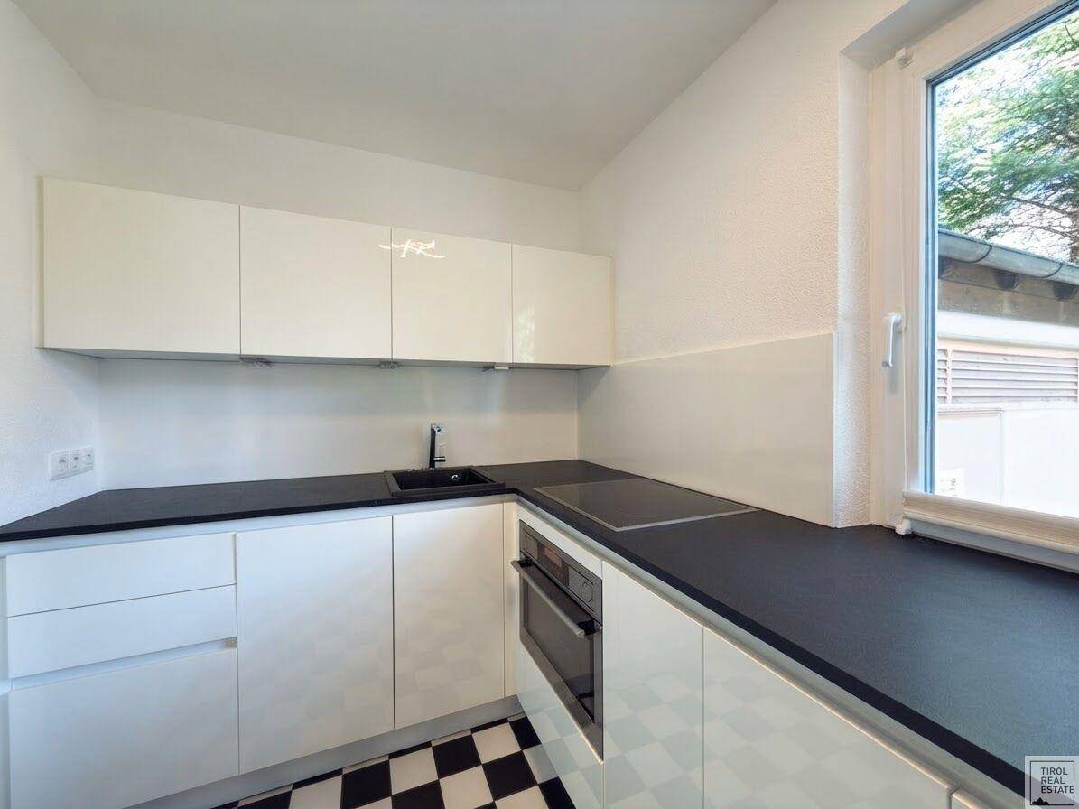 Moderne Küche mit weißen Hochglanzfronten, dunkler Arbeitsplatte und kariertem Fliesenboden.