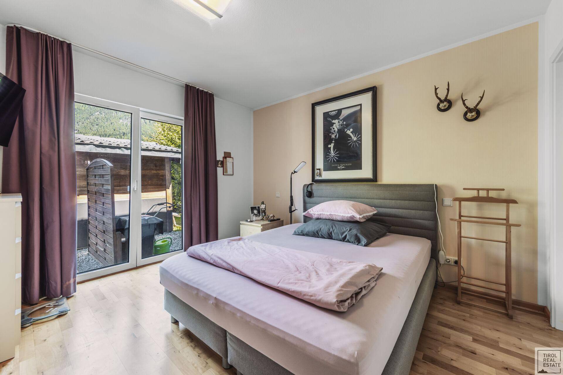 Schlafzimmer mit Doppelbett, Holzboden und Zugang zu einem kleinen Außenbereich.