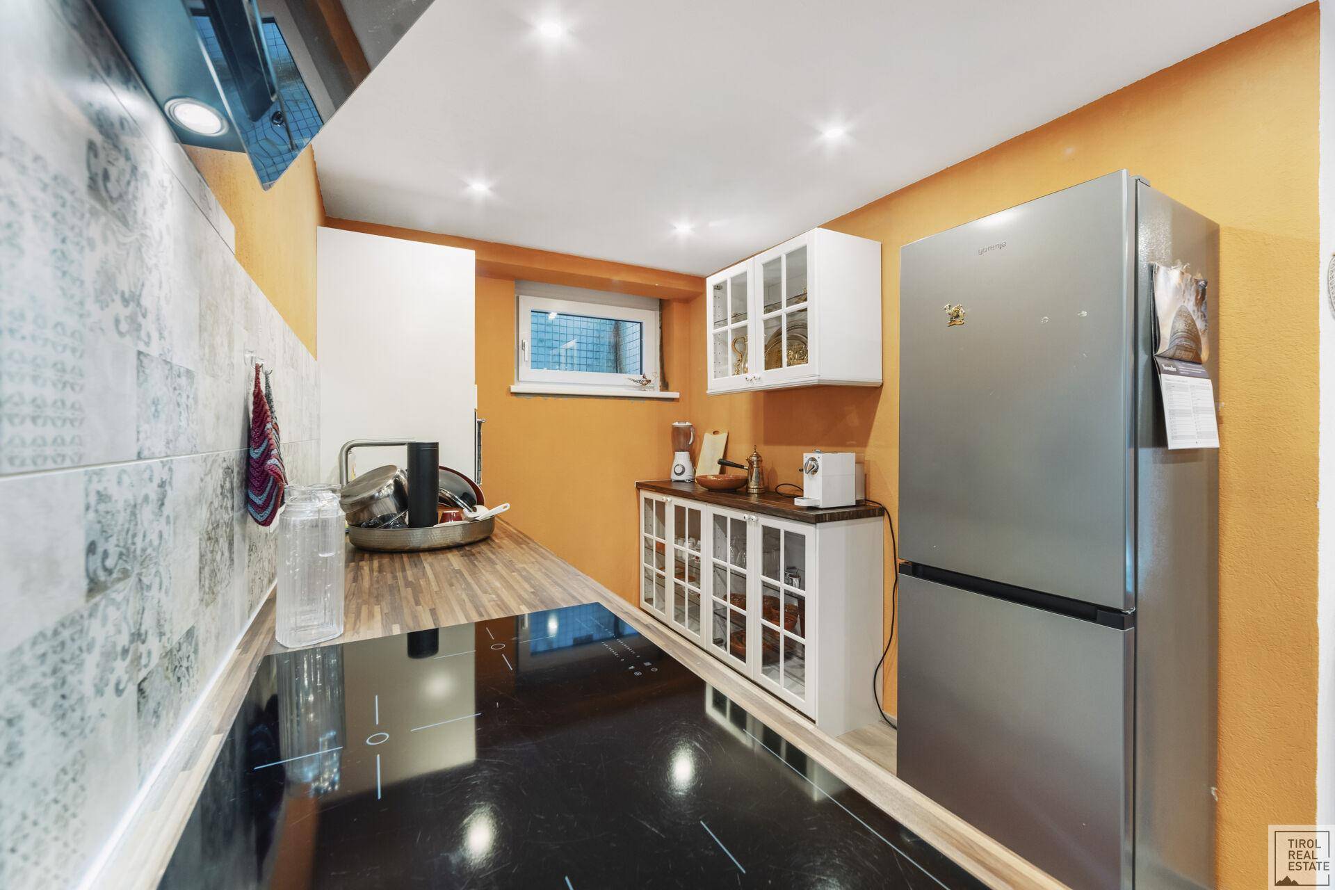 Moderne, kompakte Küche mit Induktionskochfeld, Kühlschrank und Holztheke.