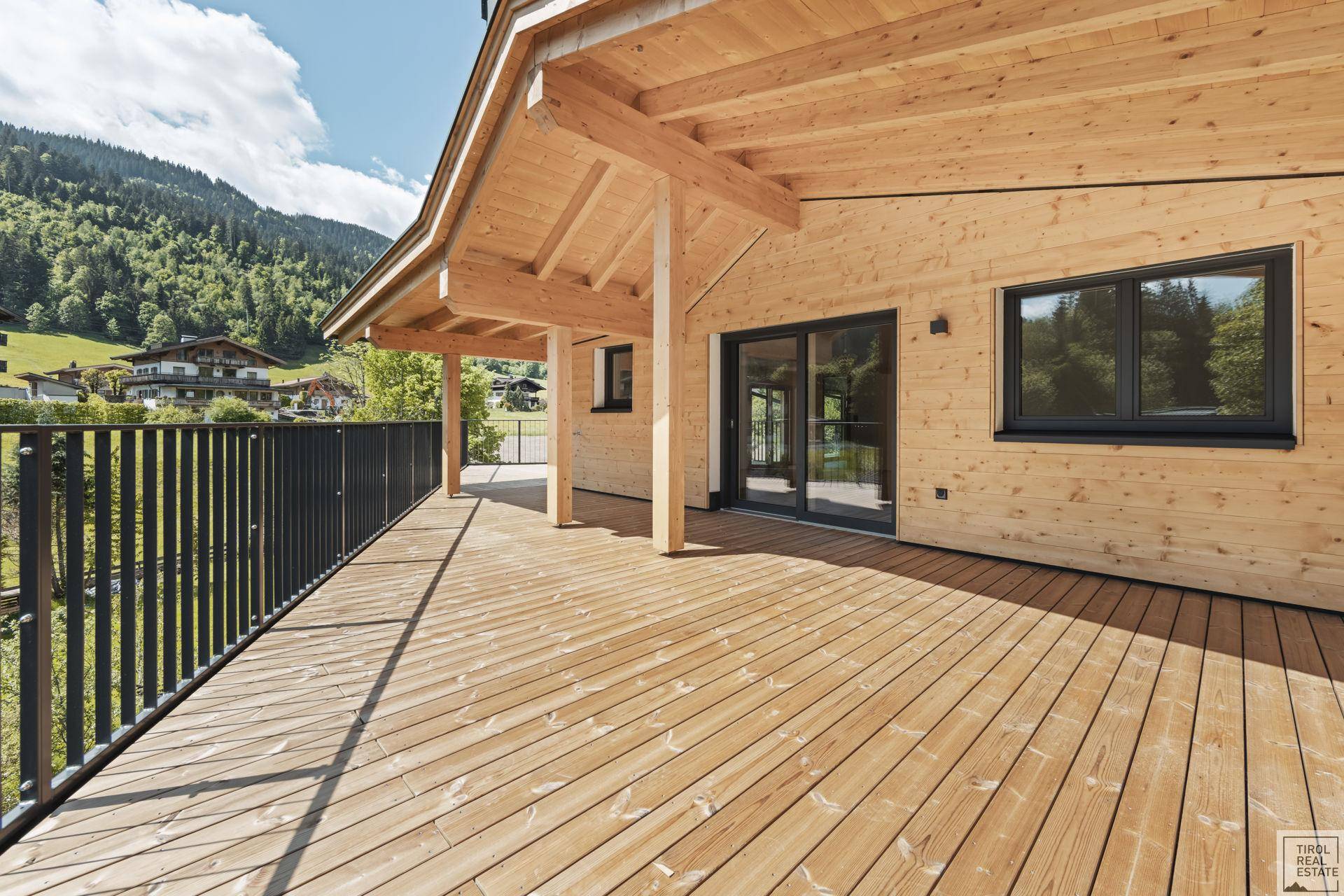 Weitläufige Holzterrasse mit schwarzem Geländer und Panoramablick auf die grüne Landschaft.