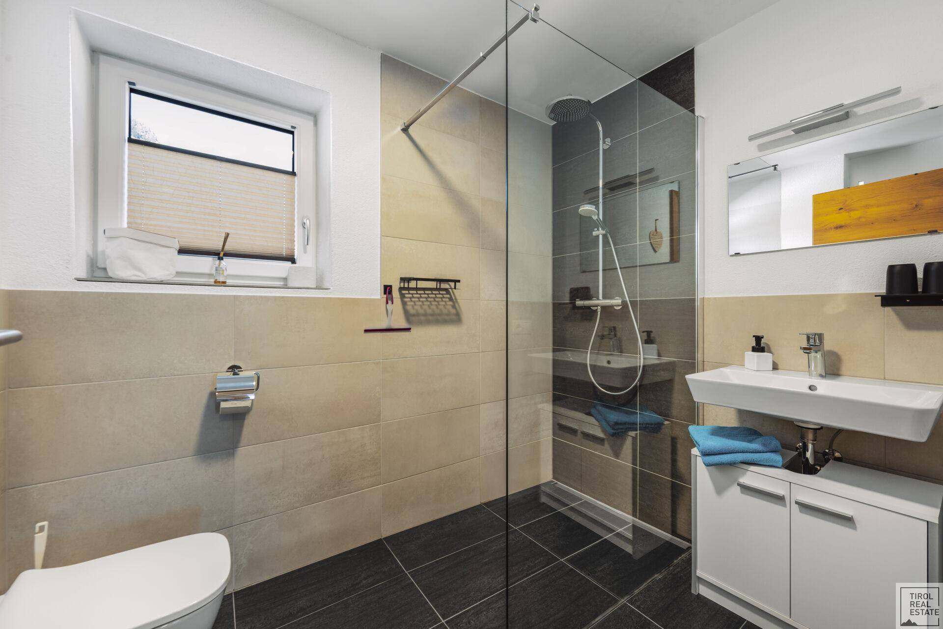 Modernes Badezimmer mit ebenerdiger Dusche, Fenster und dunklen Bodenfliesen.