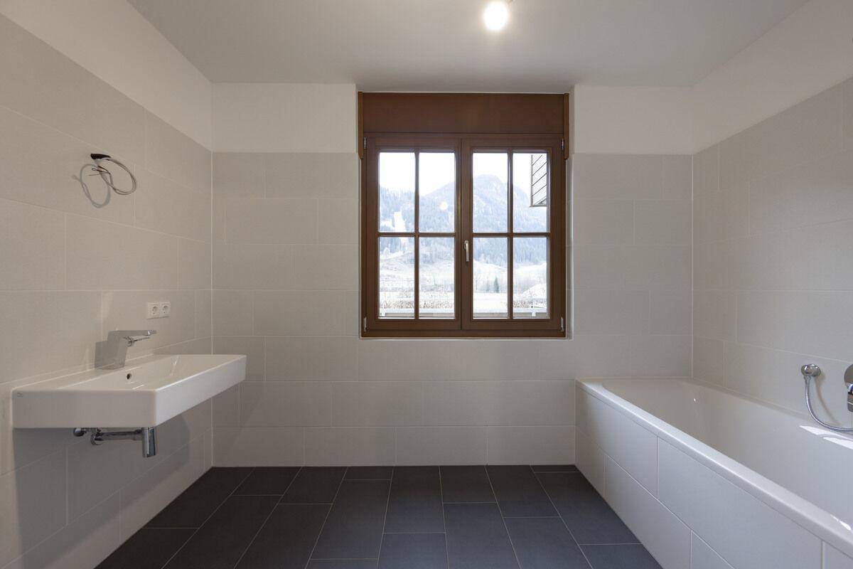 Helles Badezimmer mit Waschtisch, Badewanne, Fliesen und Fenster mit Bergblick.